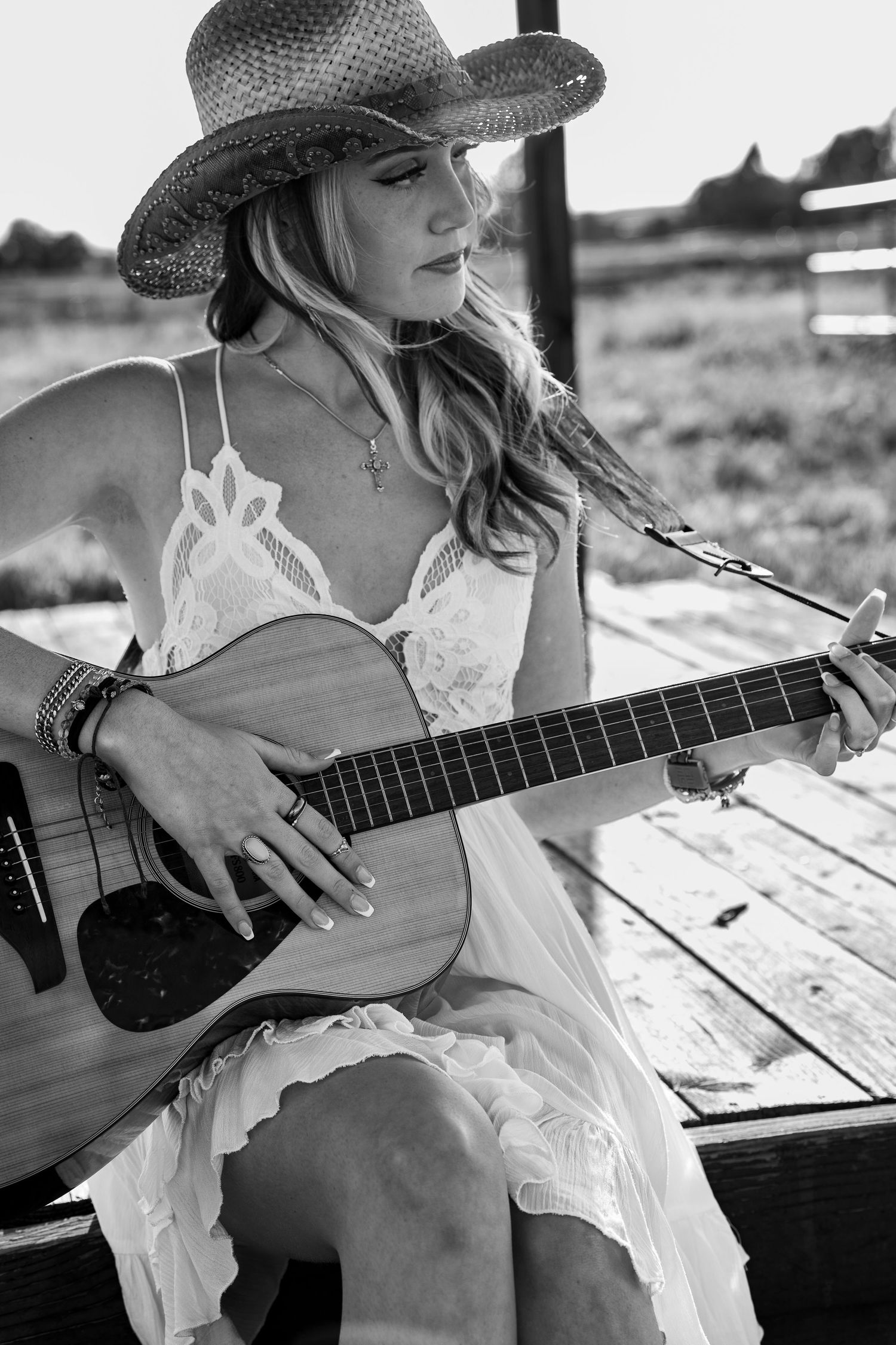 Black and white series of someone playing acoustic guitar while wearing a sun hat on wooden deck.