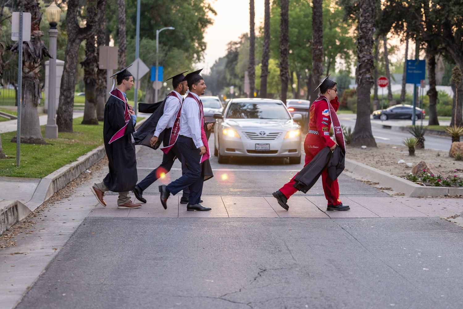 People walking down a tree-lined street carrying luggage and bags during daytime.