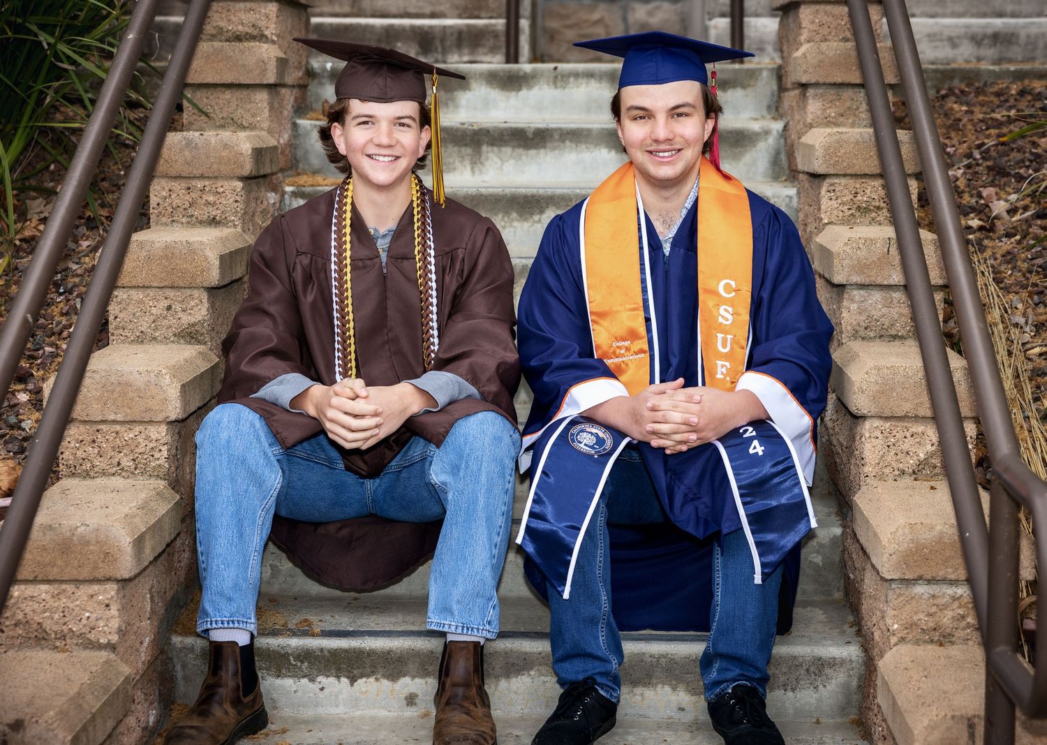 Graduates in blue caps and gowns sit on stone steps during graduation photo session.