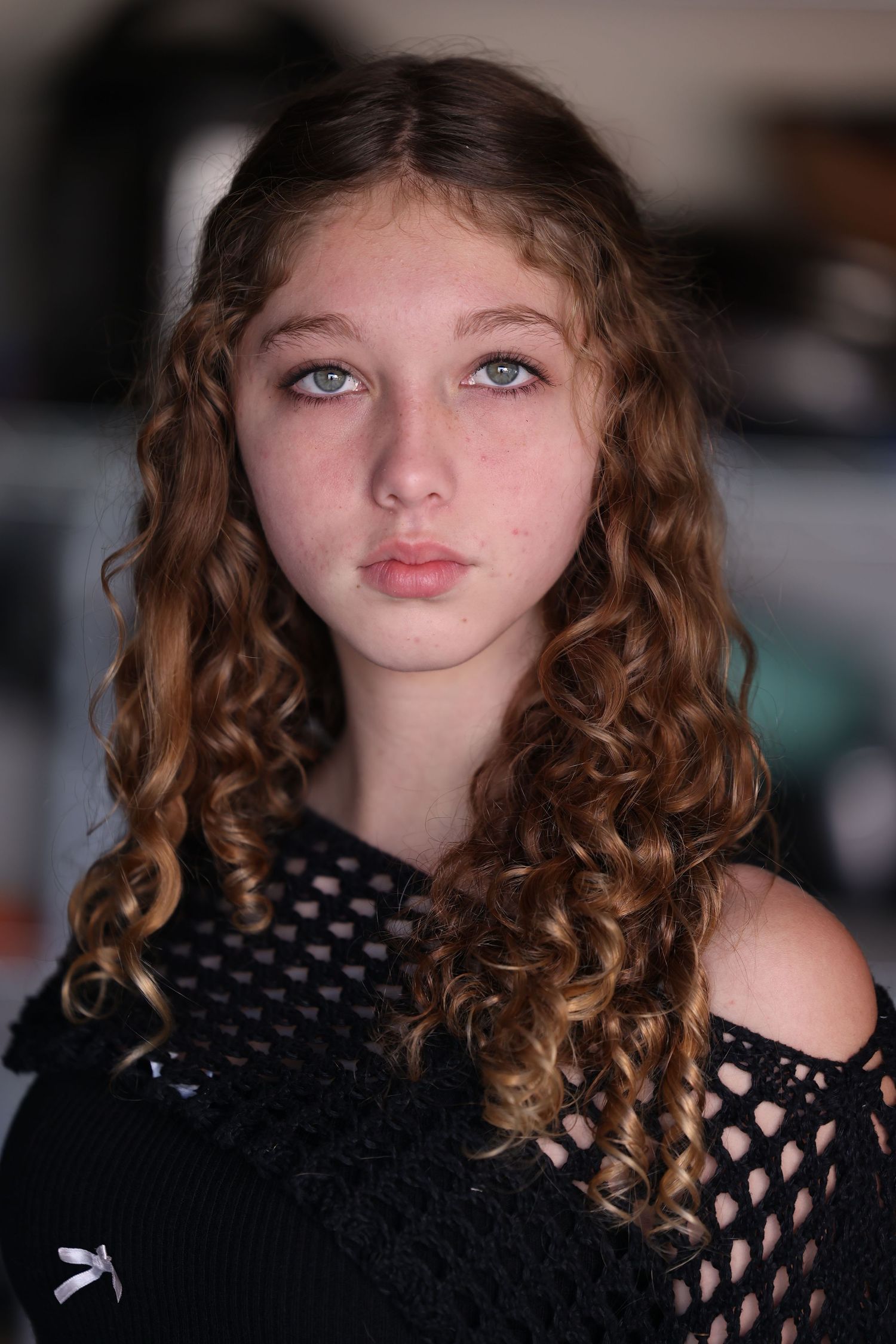 Portrait in black mesh top with curly hair against dark background.
