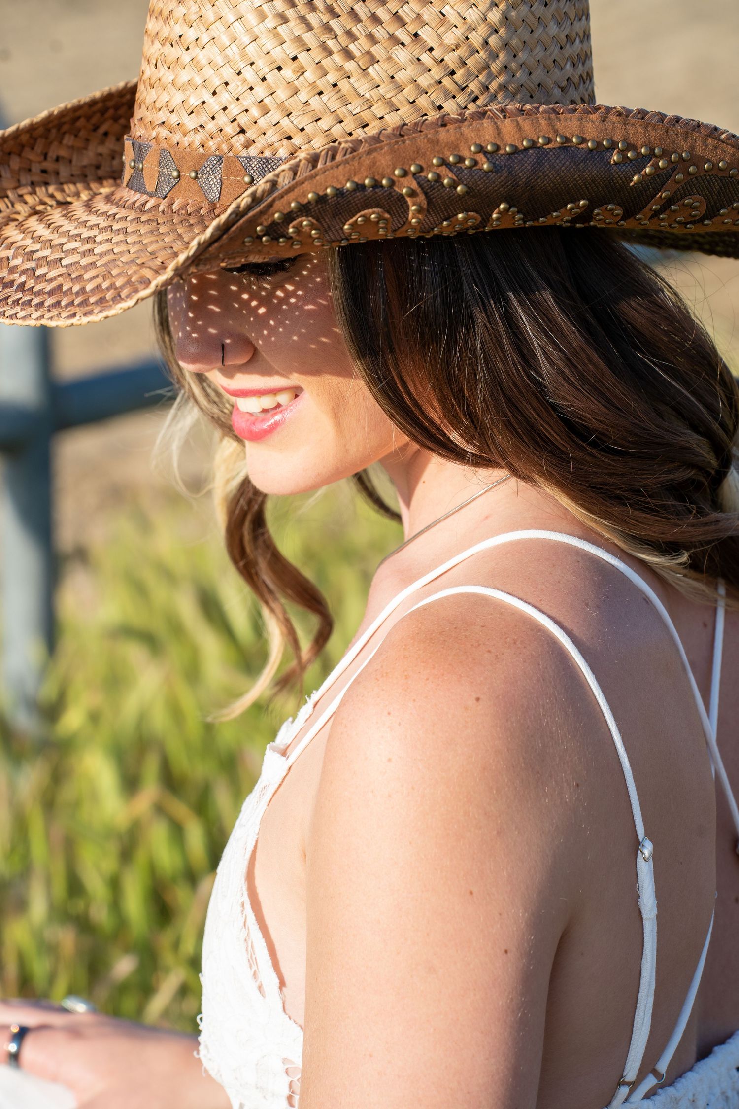 Woman in white top and straw hat enjoying golden hour sunlight at a rustic outdoor location.