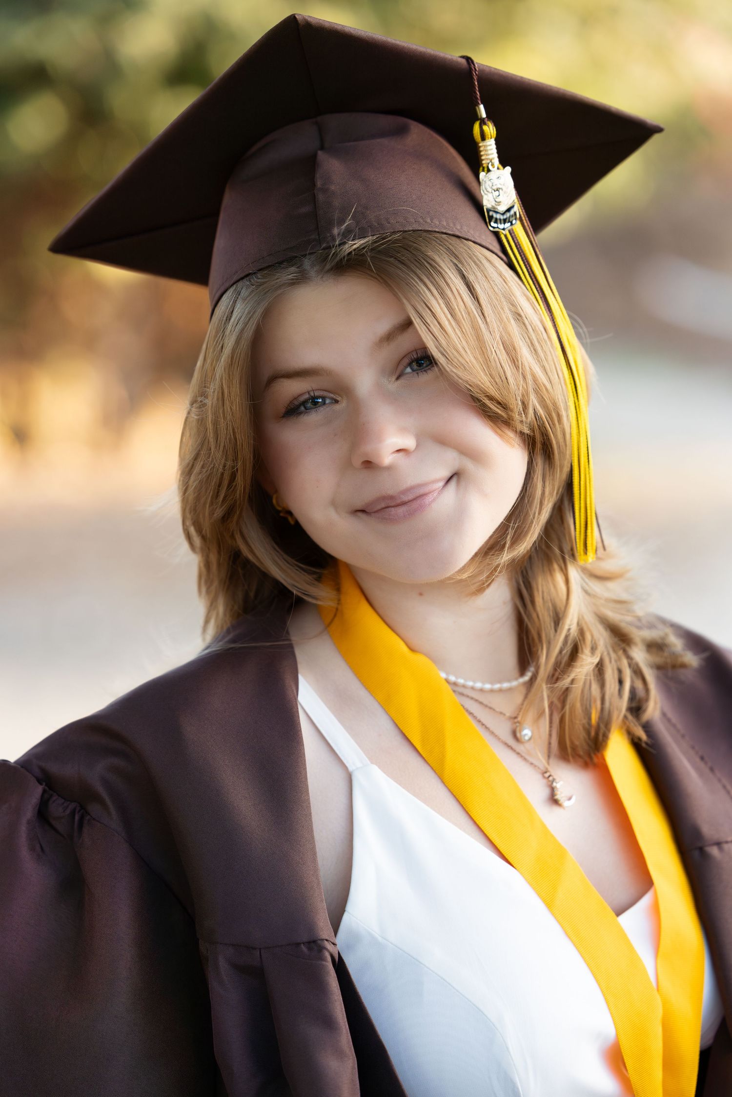 Graduate in cap and gown with yellow tassel smiling in outdoor portrait session.