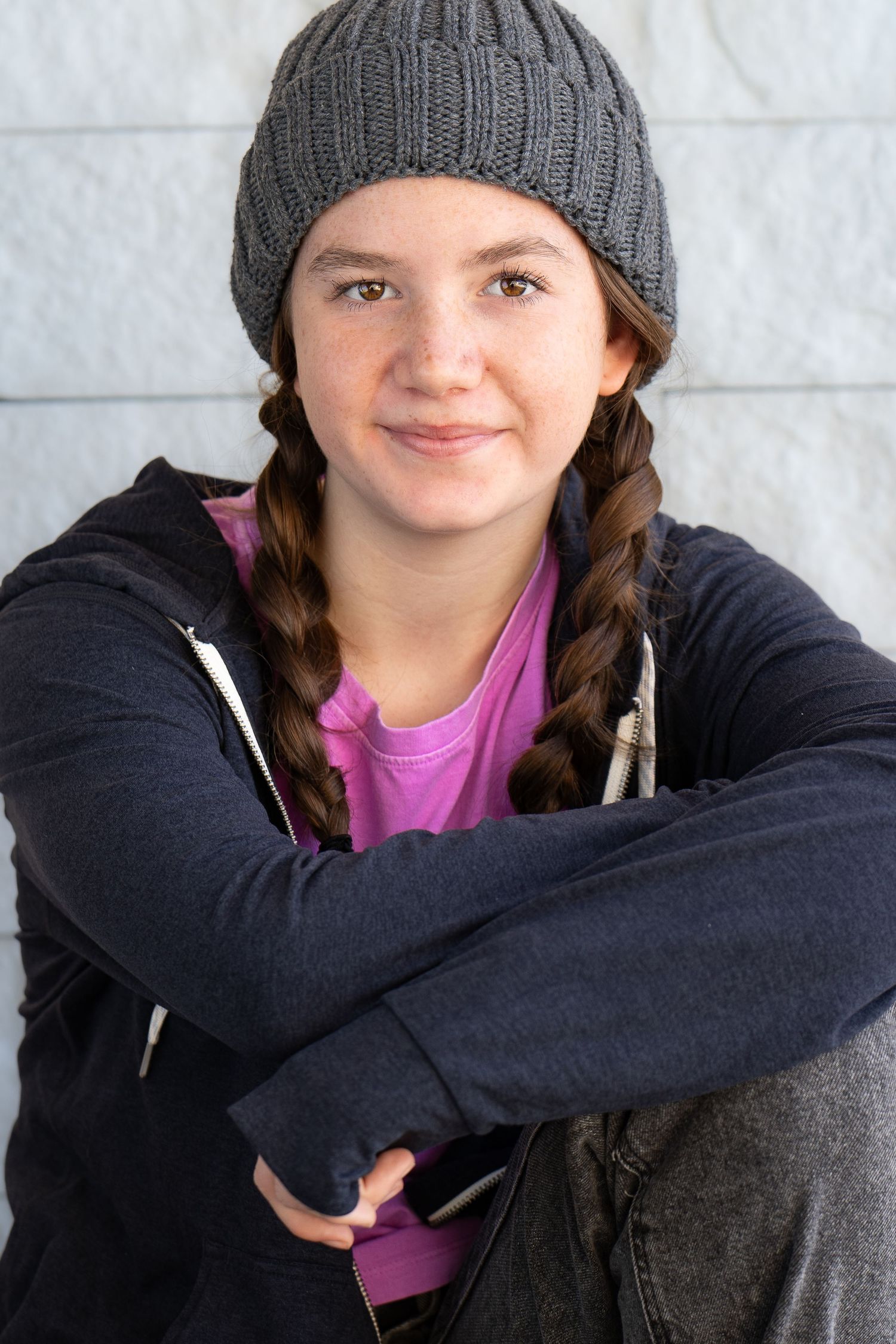 A tween headshot in a gray knit beanie and black hoodie sits casually with braided hair and a purple shirt underneath.