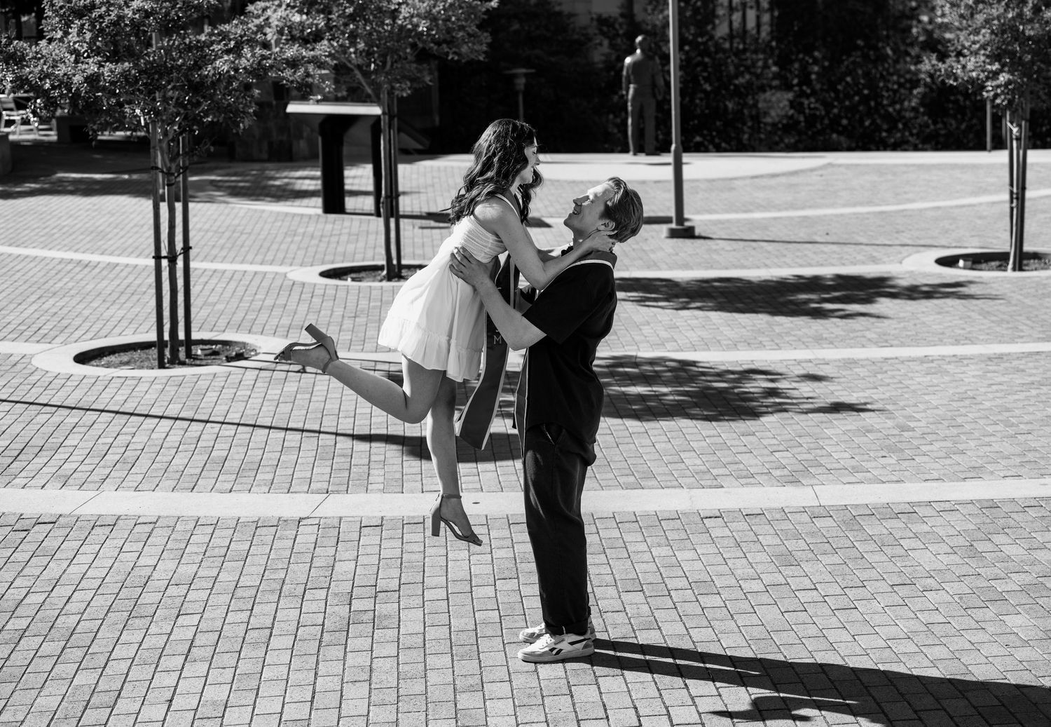 Black and white photo series showing a couple dancing together in a public square with brick pavement.