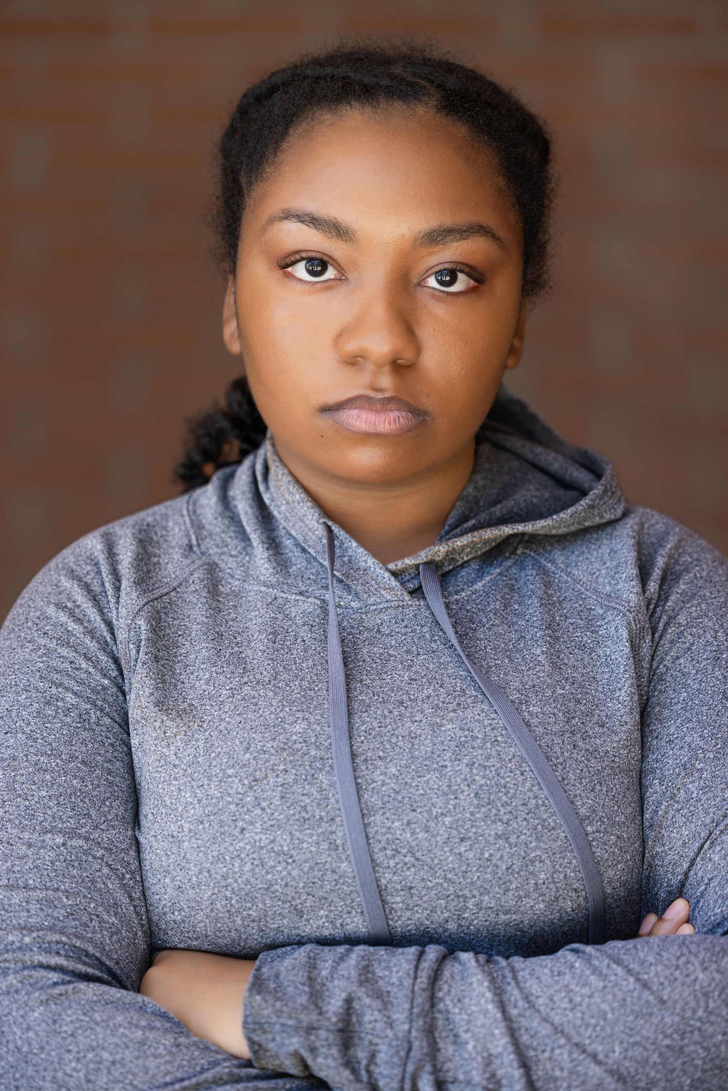 Casual portraits in grey hoodie against brick wall background.