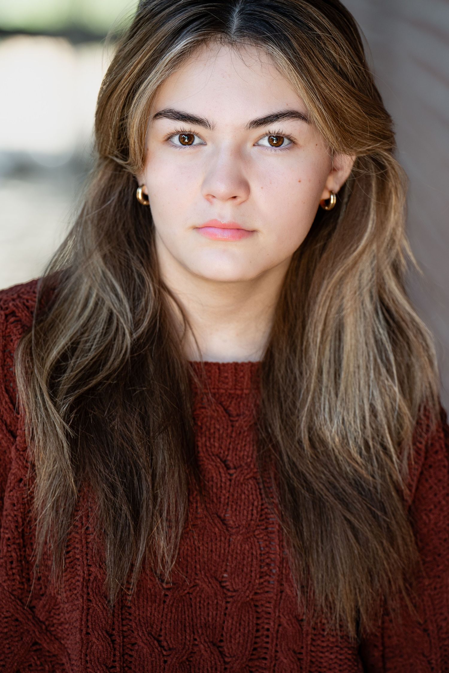 A close-up portrait of someone in a maroon knit sweater with long brown hair against a blurred background.