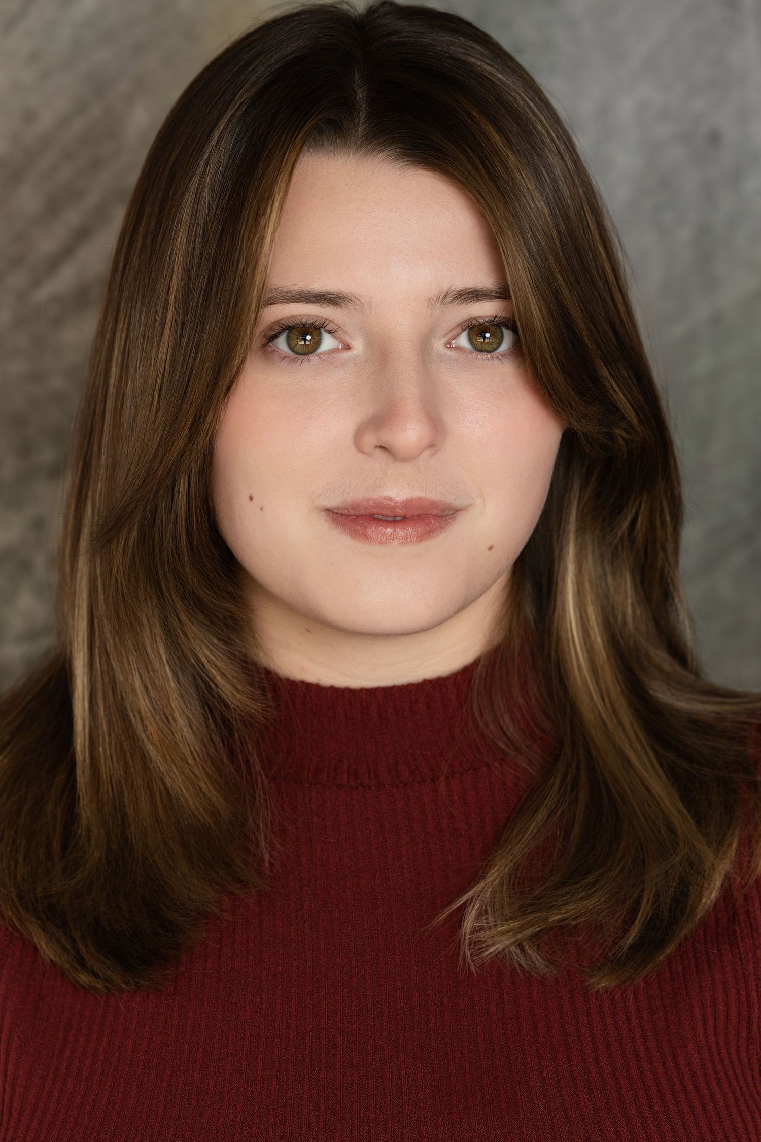 Portrait view in dark burgundy turtleneck sweater against grey backdrop.