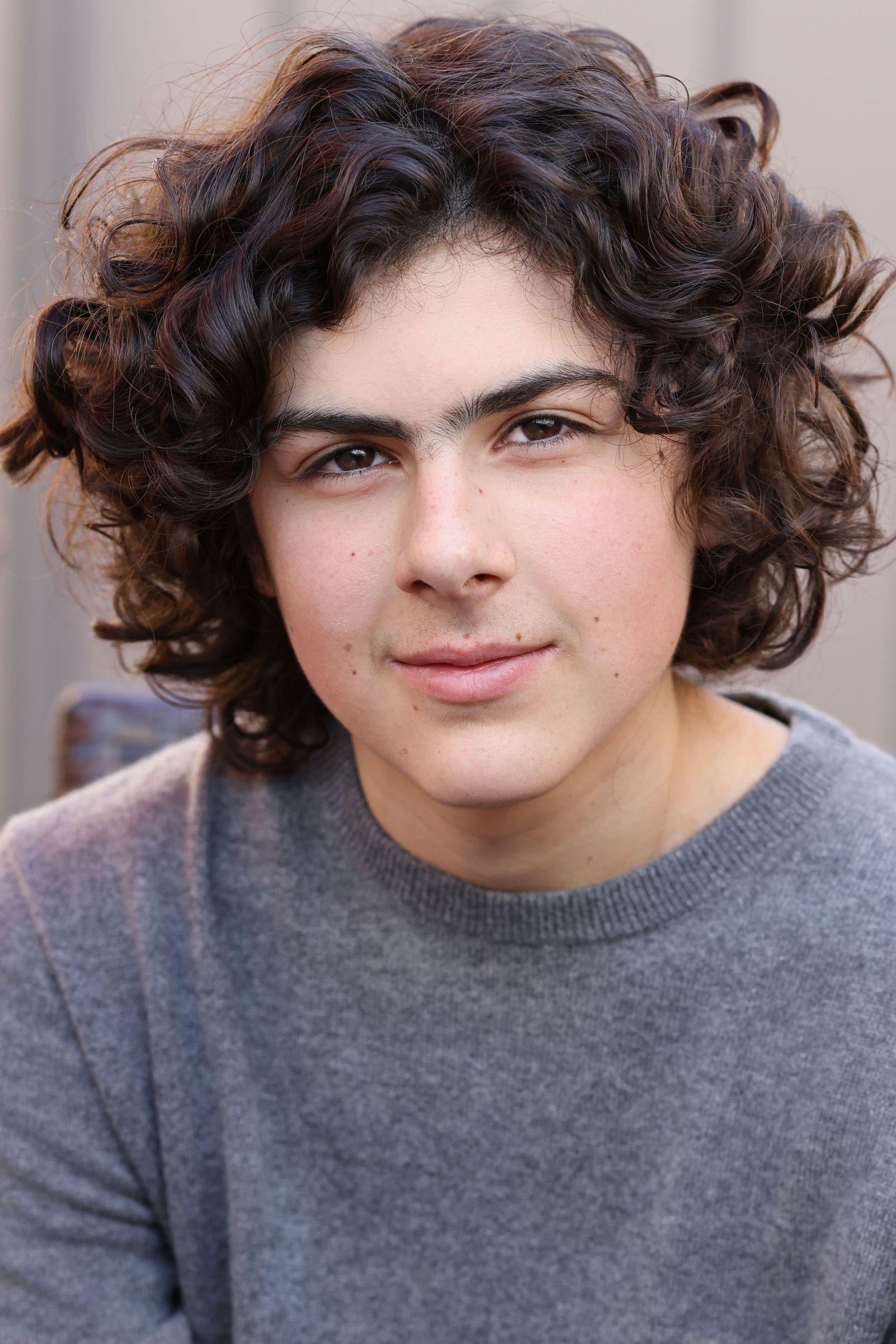 Four portrait photos of a person with curly dark hair wearing a grey sweater displaying various playful expressions.