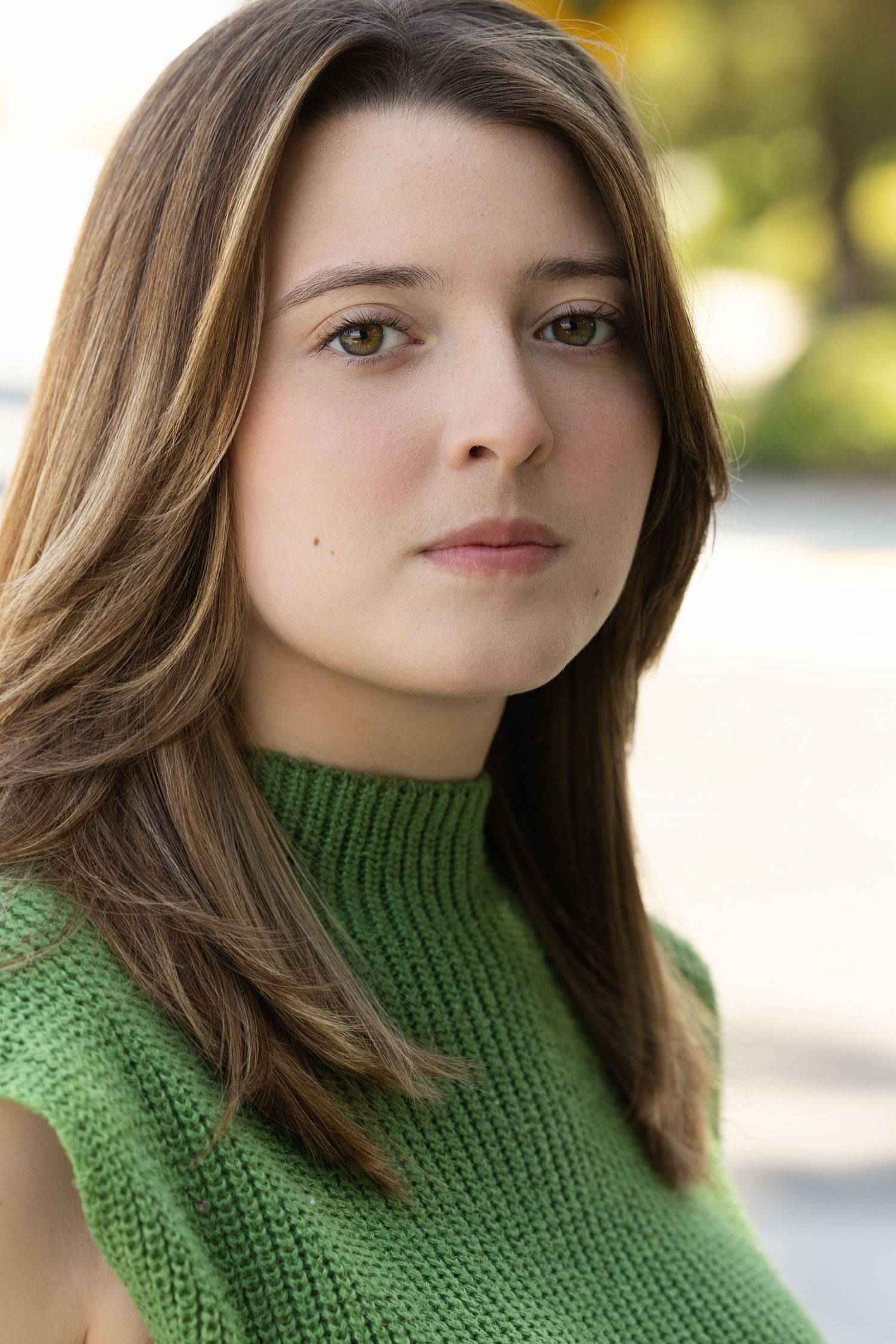 An individual wearing a cozy green turtleneck sweater poses confidently against a soft blurred background in natural light.
