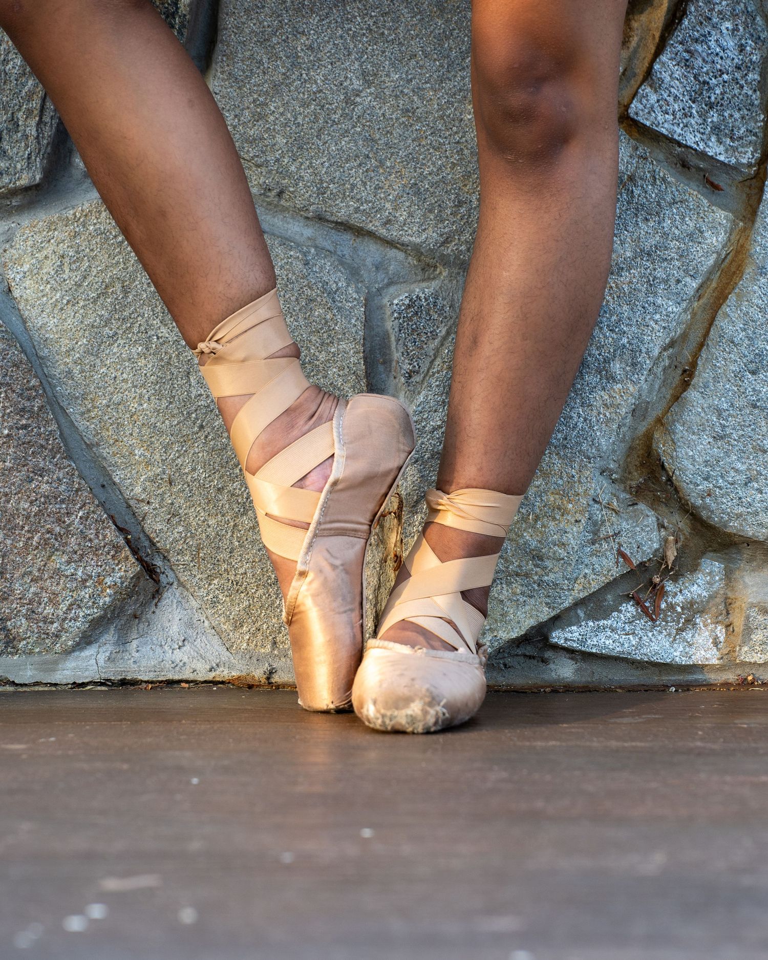 Ballet dancer's feet in pink pointe shoes performing various positions against a stone wall with dramatic lighting.