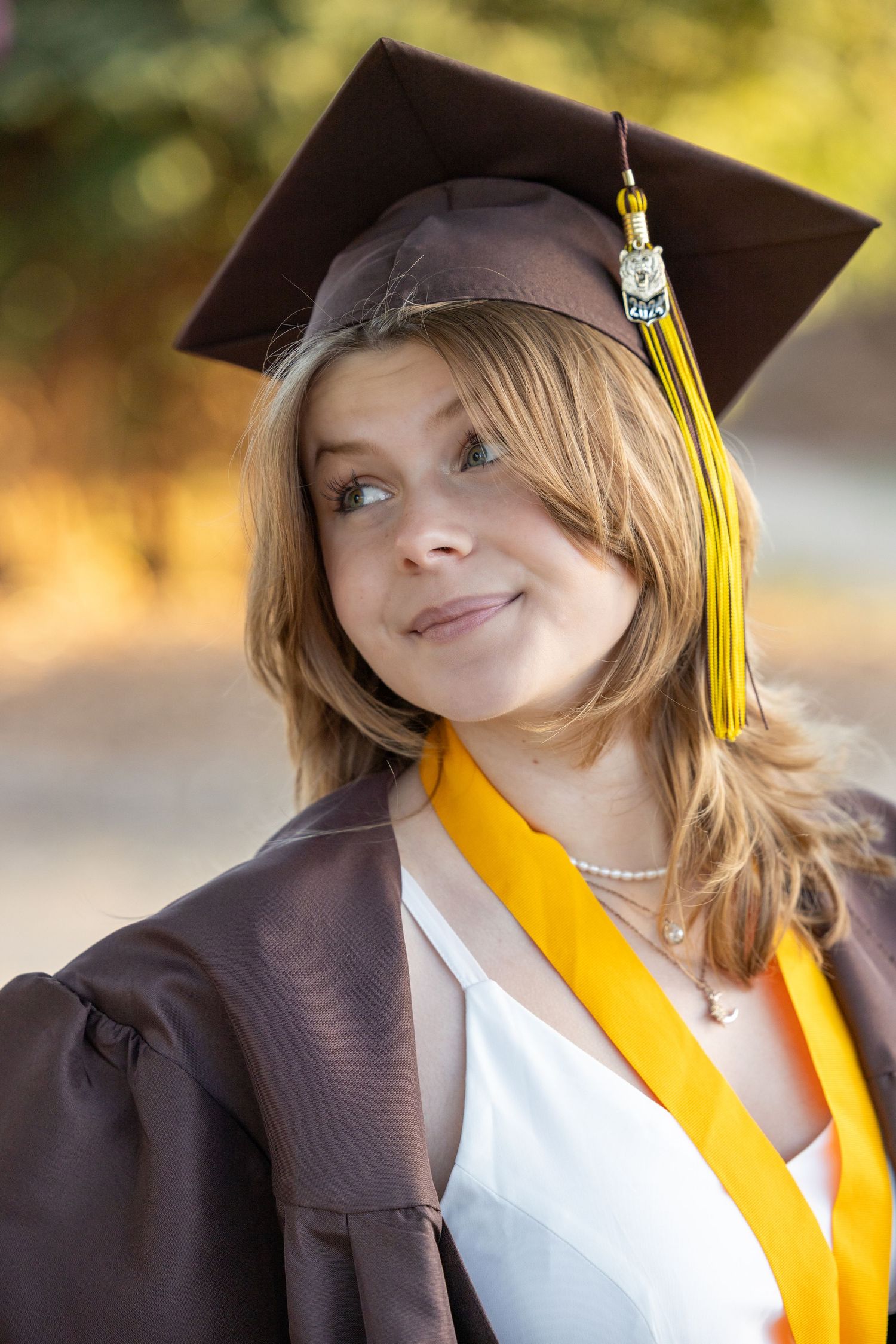 Graduate in cap and gown with yellow tassel smiles during outdoor graduation photo session.