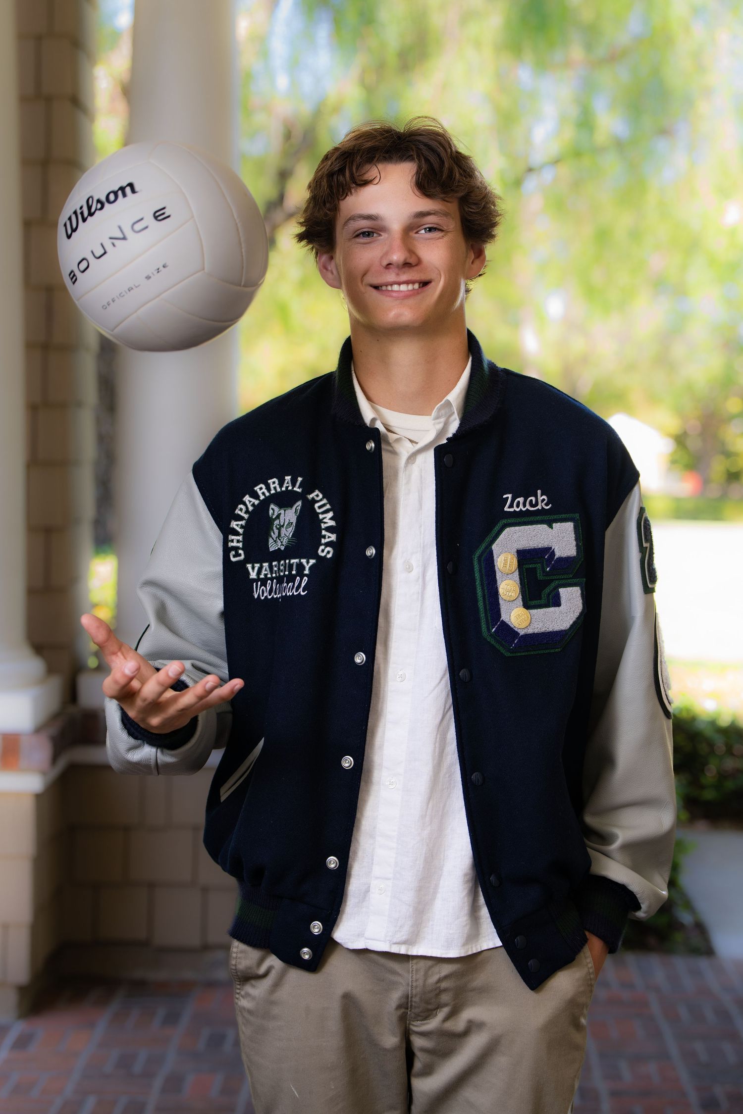 Teen boy named Zack in Chaparral Pumas varsity volleyball letterman jacket tossing a Wilson volleyball outdoors.