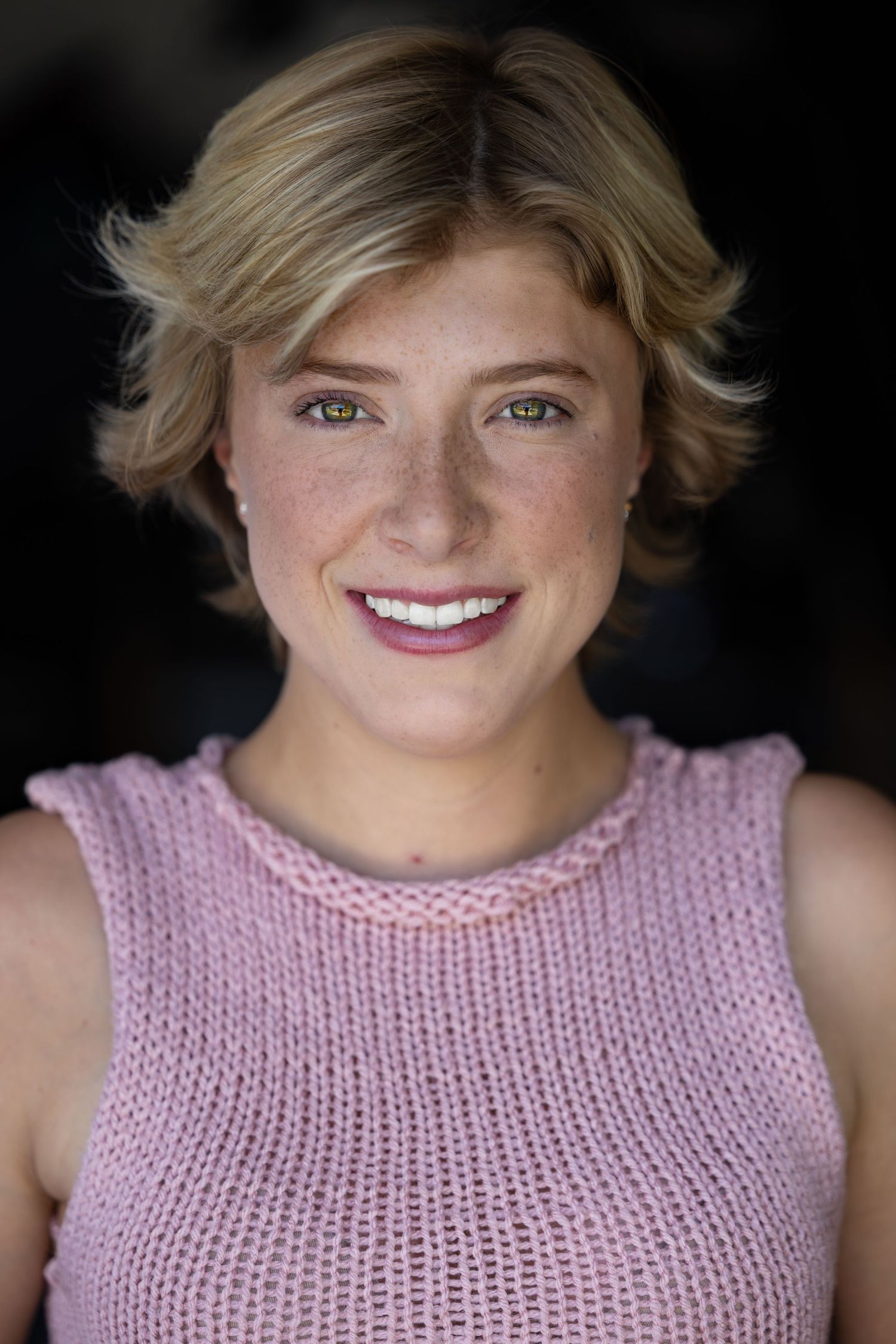 headshot of someone wearing a pink knit sleeveless sweater with a bright smile.