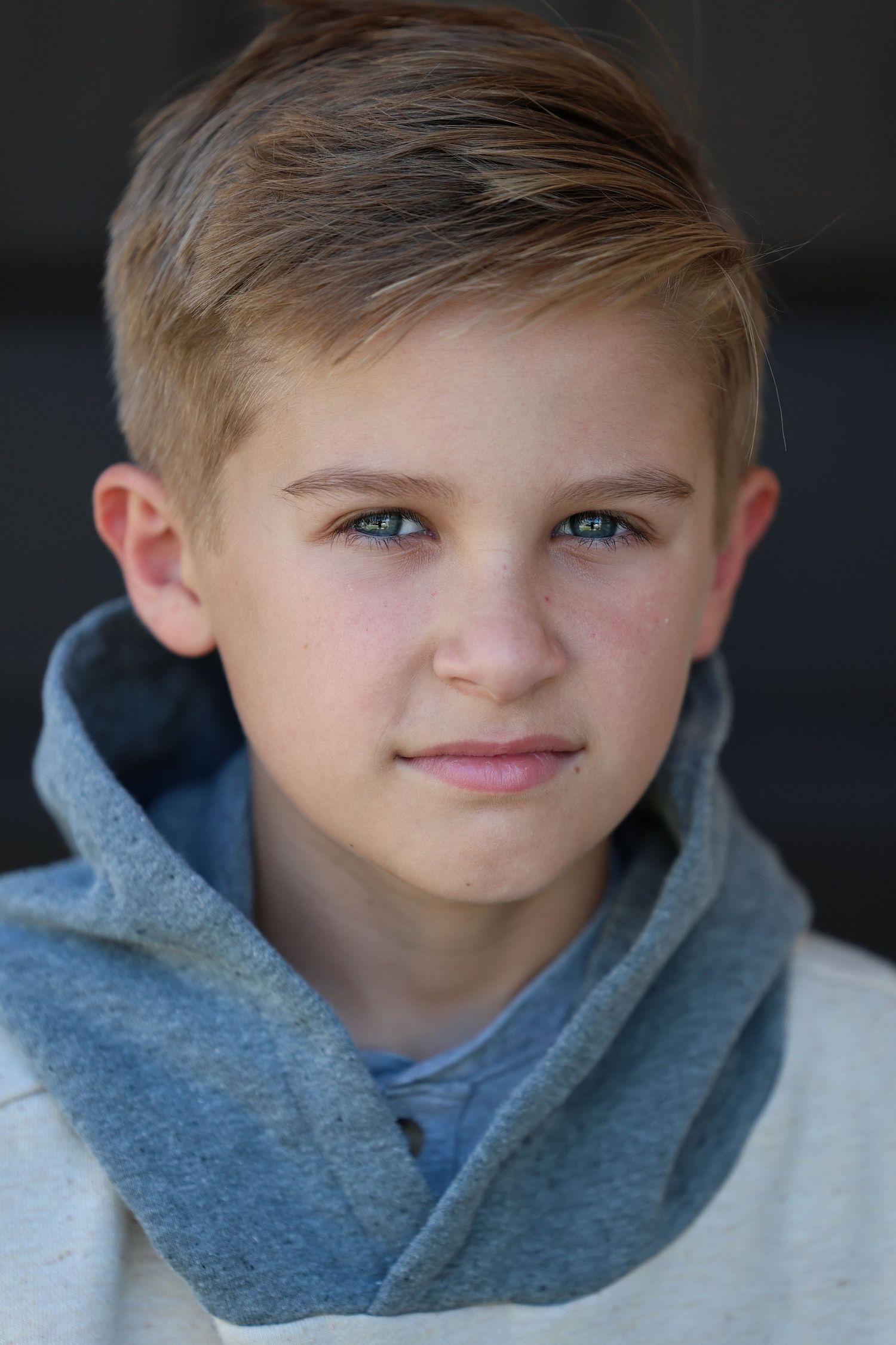 A young person wearing a gray hoodie poses for five progressive closeup shots against a dark background, showing a playful expression.