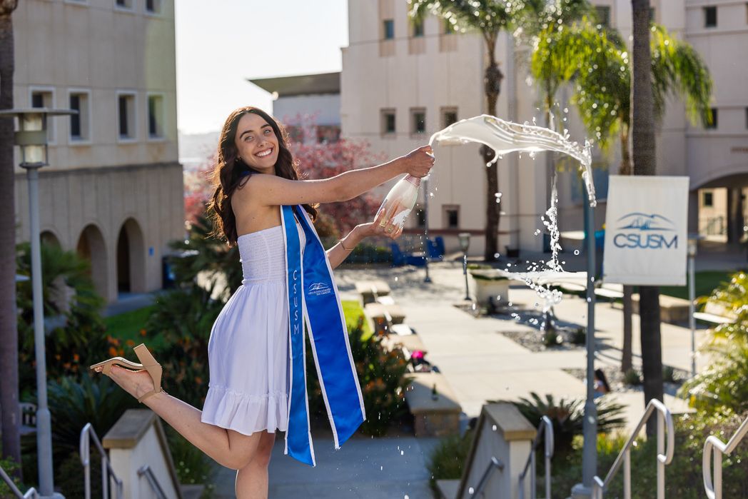 A group of dancers in white dresses with blue sashes perform in a sunny Mediterranean courtyard setting.