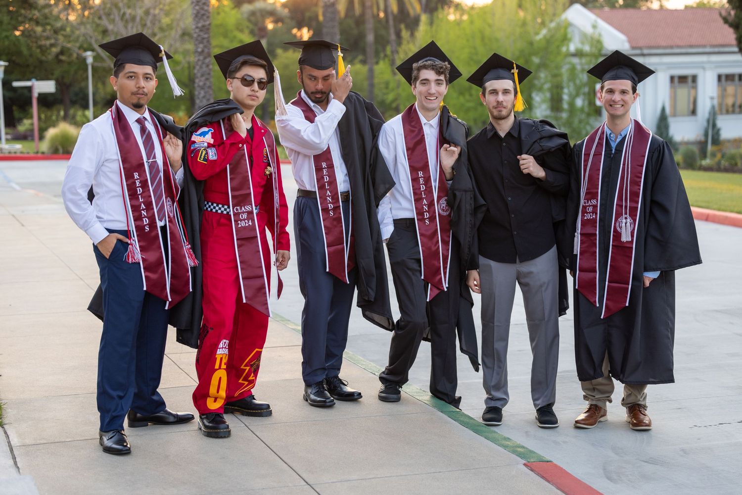 Group of graduates wearing red and white stoles posing together outside a building.