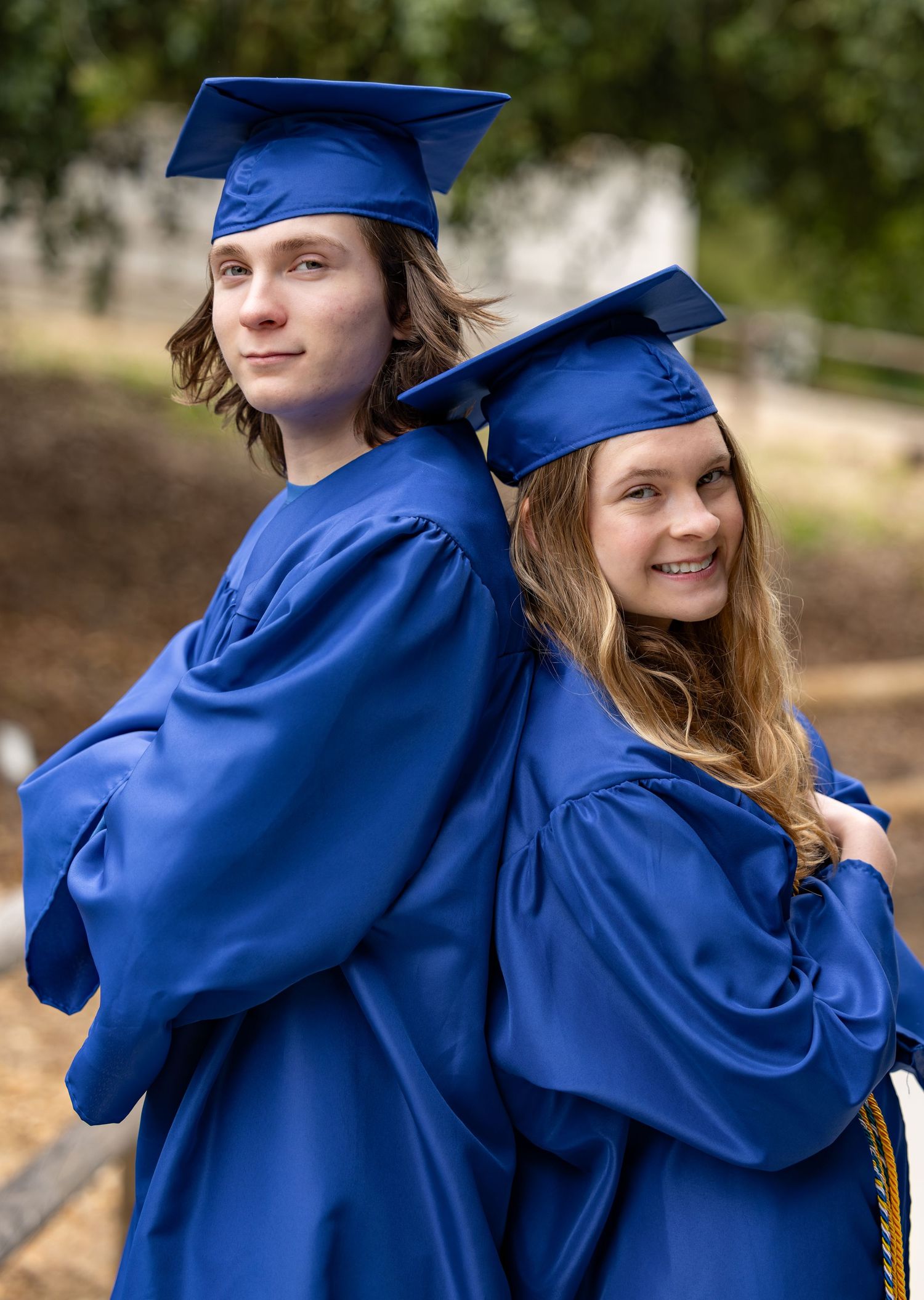 Graduates in royal blue caps and gowns embrace and celebrate during outdoor commencement ceremony.