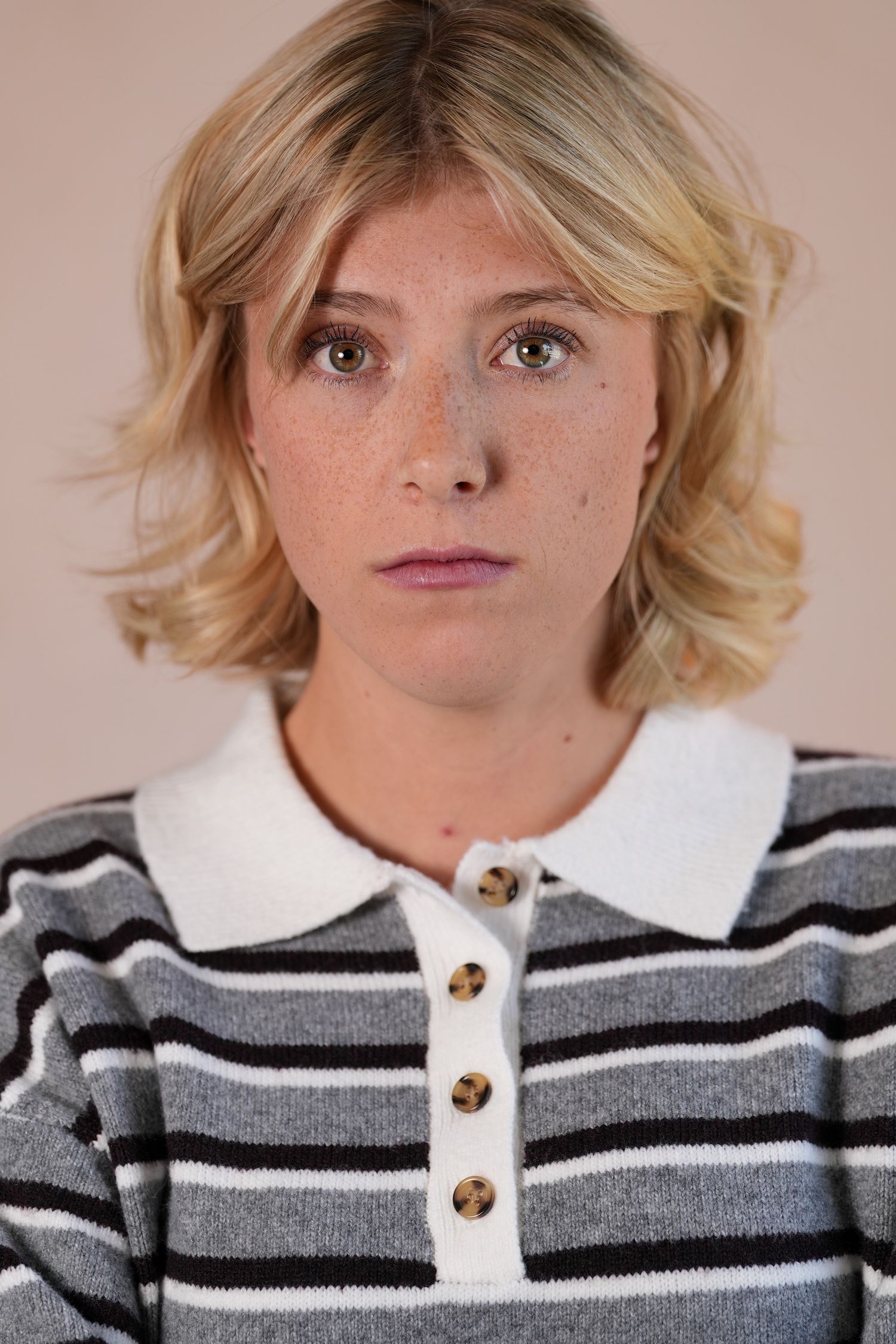 Young blonde woman with freckles wearing a gray striped polo sweater, looking directly at camera.