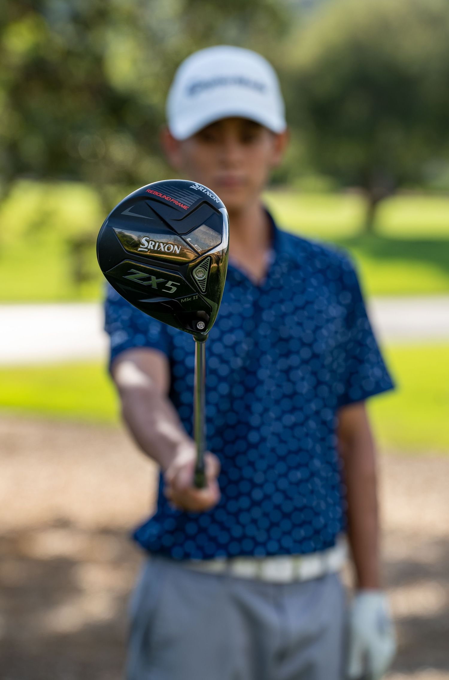 Close up of a black TaylorMade golf driver club head against blurred green background.
