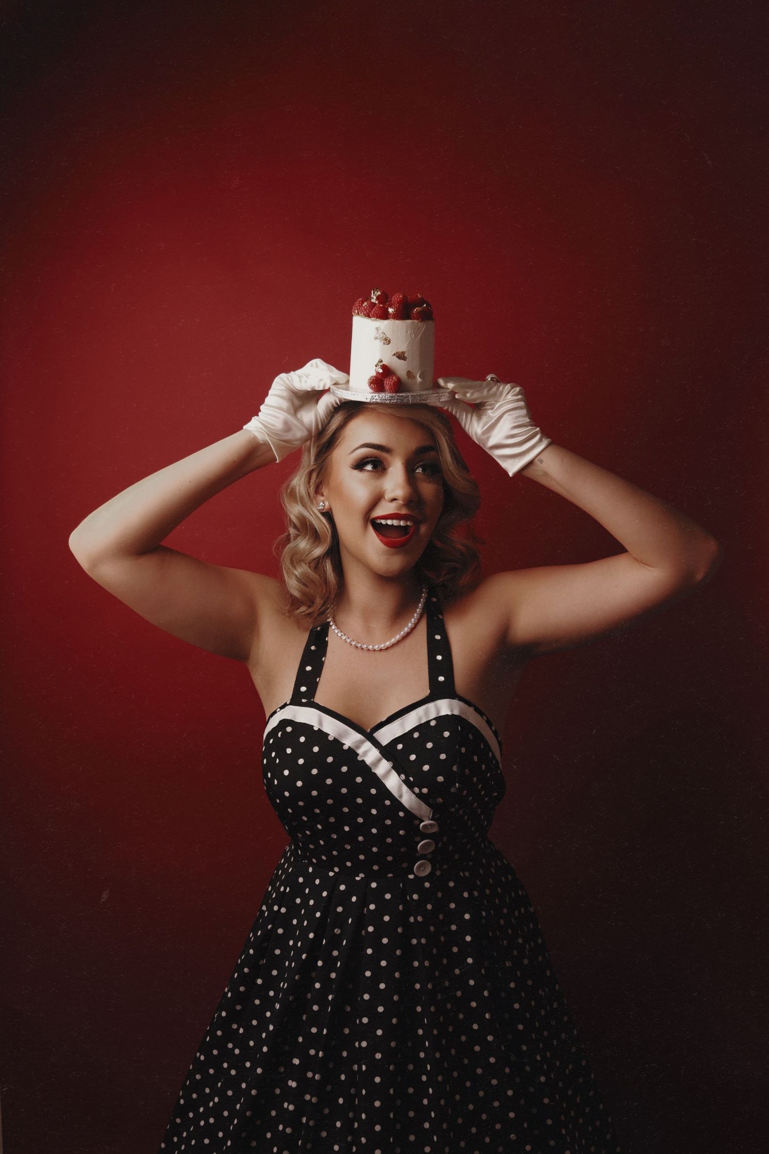 Dramatic portrait in a polka dot dress with vintage styling against a red backdrop.