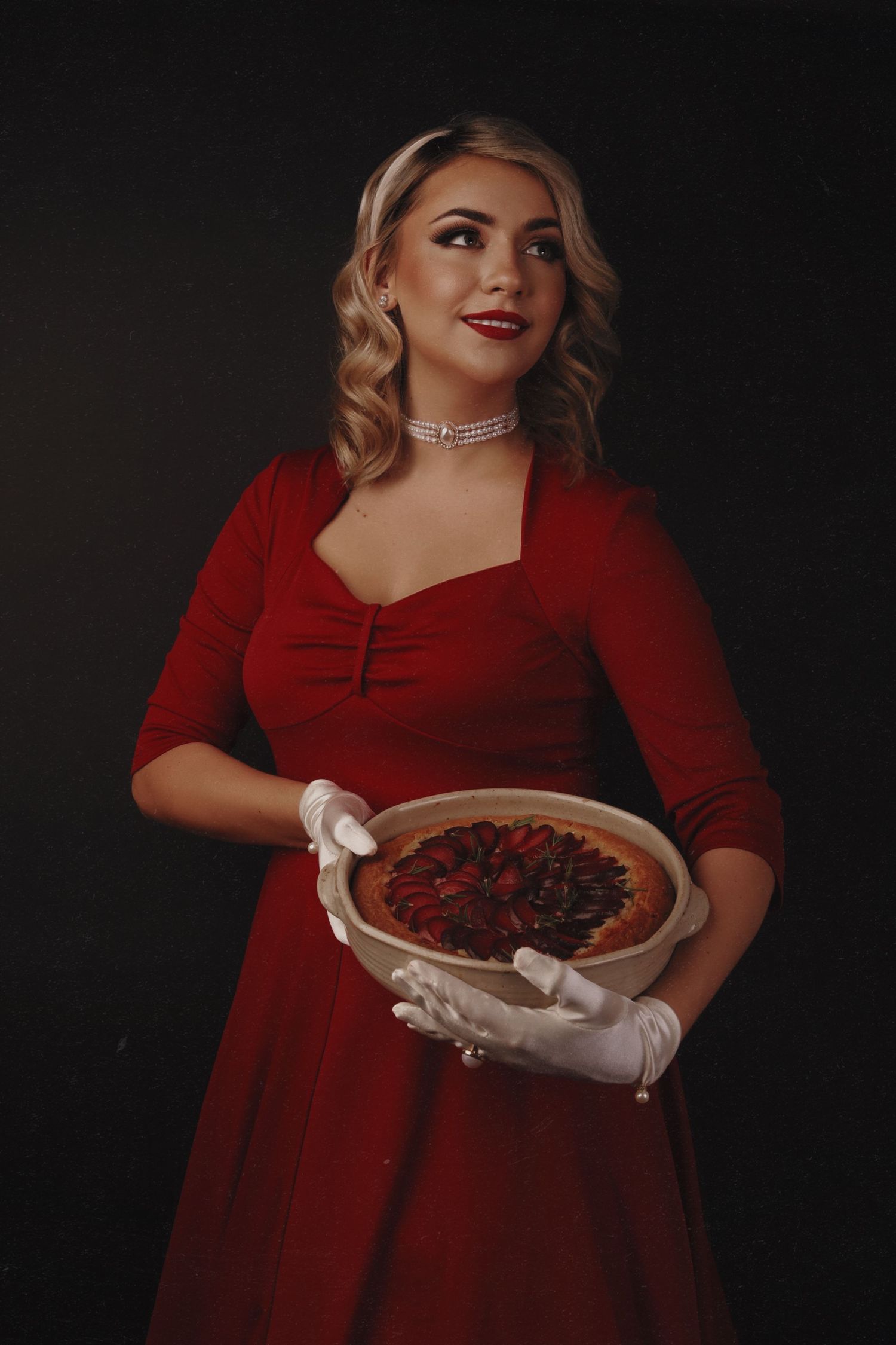 A red-dressed figure holds a platter while wearing white gloves against a dark background.