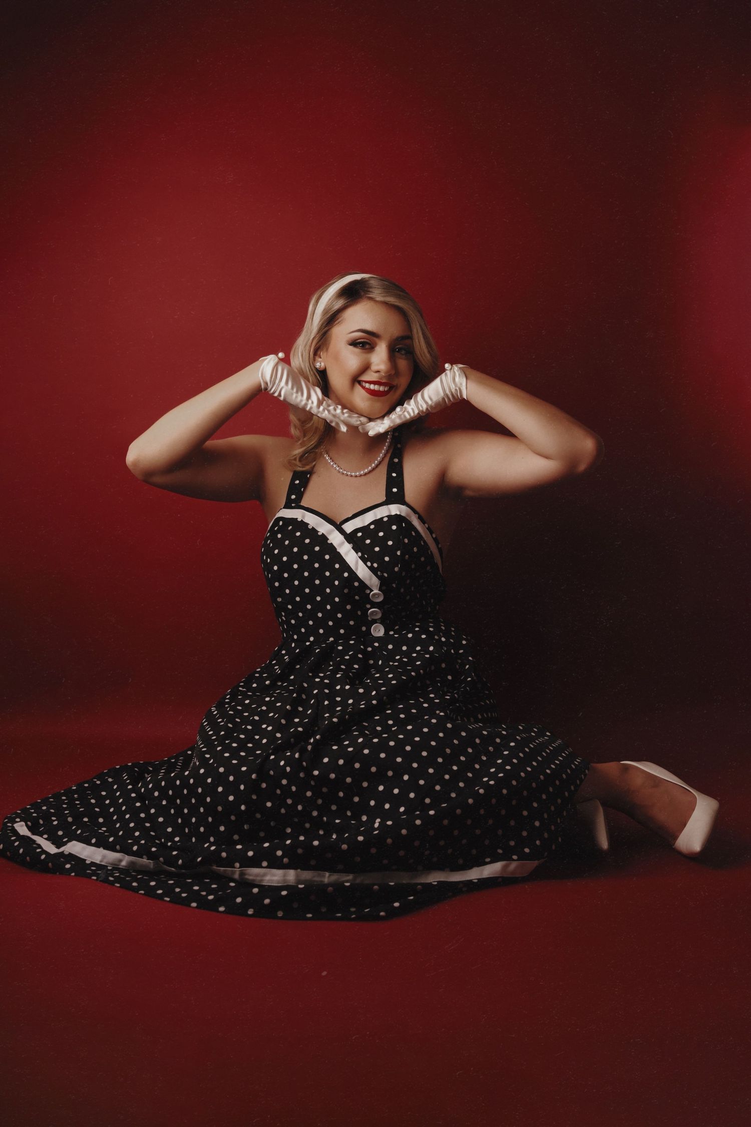 Artistic photo of someone reclining in a black and white polka dot dress on a red background.