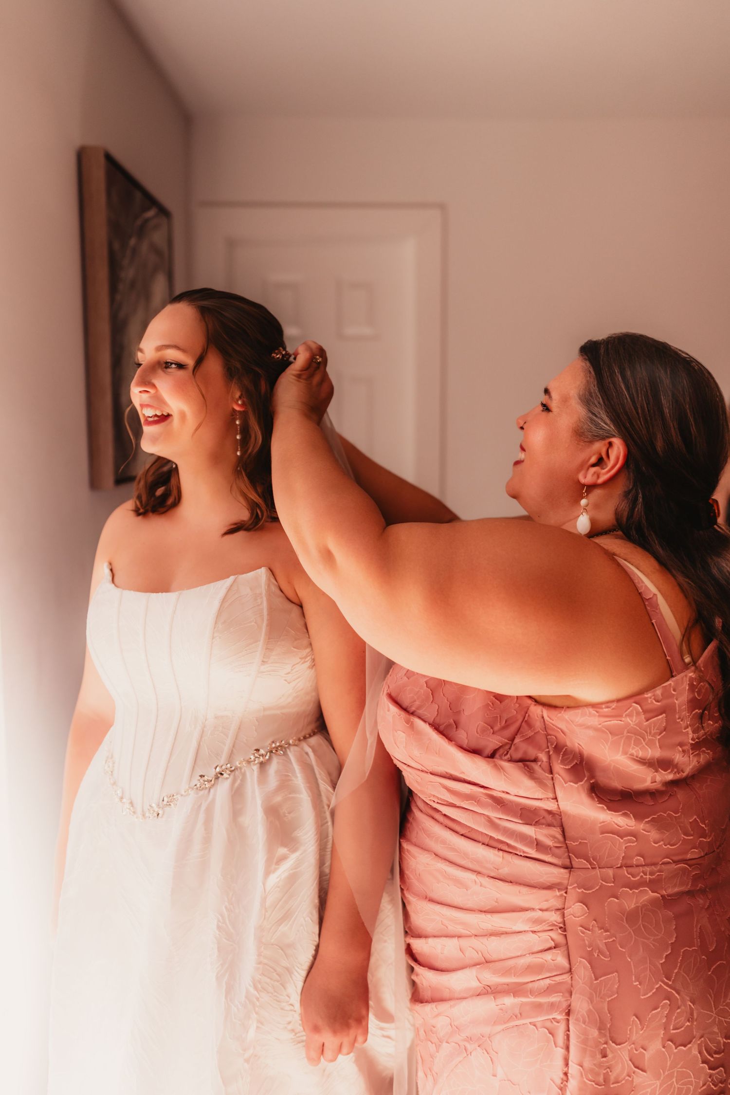 Mother helps bride with hair accessories as she prepares in white strapless gown before wedding ceremony.