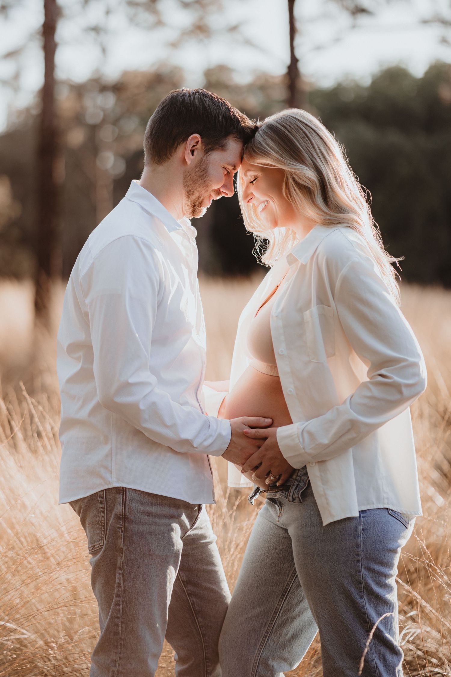 Expecting couple touching foreheads lovingly in golden wheat field at sunset.