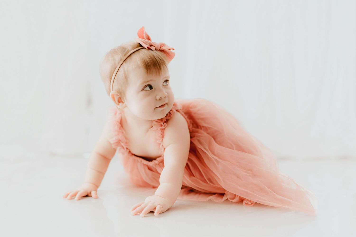 Curious baby girl in dusty rose tulle dress looks up while crawling.