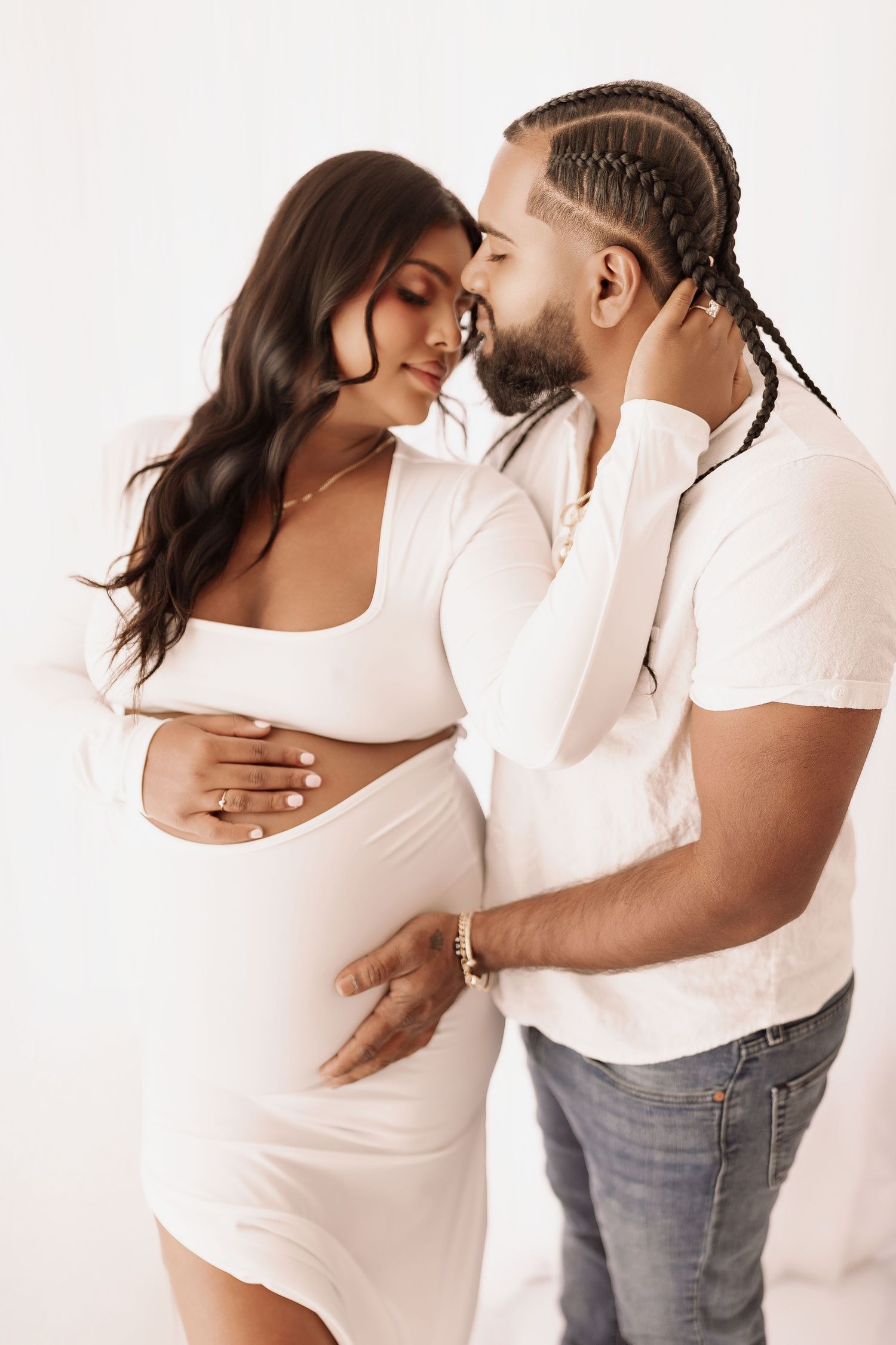 Couple sharing tender moment, pregnant woman in white dress with partner kissing her forehead.