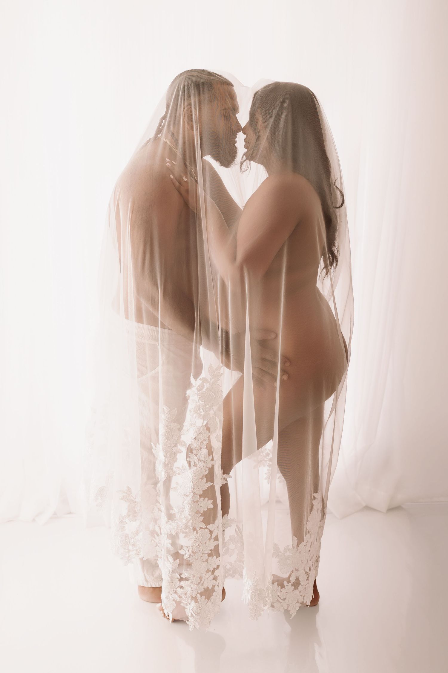 Couple sharing intimate moment covered by sheer white floral lace wedding veil.
