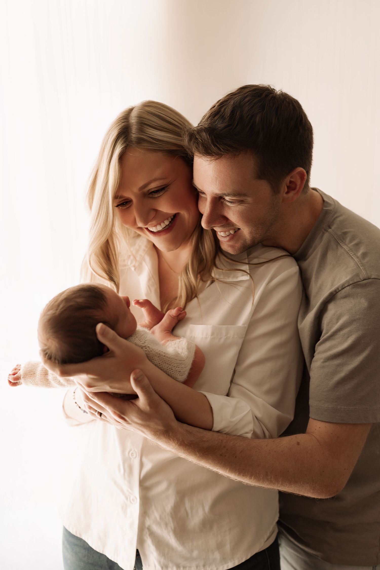 Happy young couple smiling together while cradling their newborn baby in a bright studio.