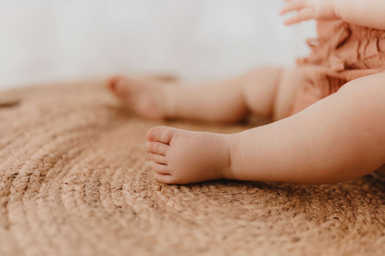 Close-up of tiny newborn baby feet resting on a natural woven jute rug.