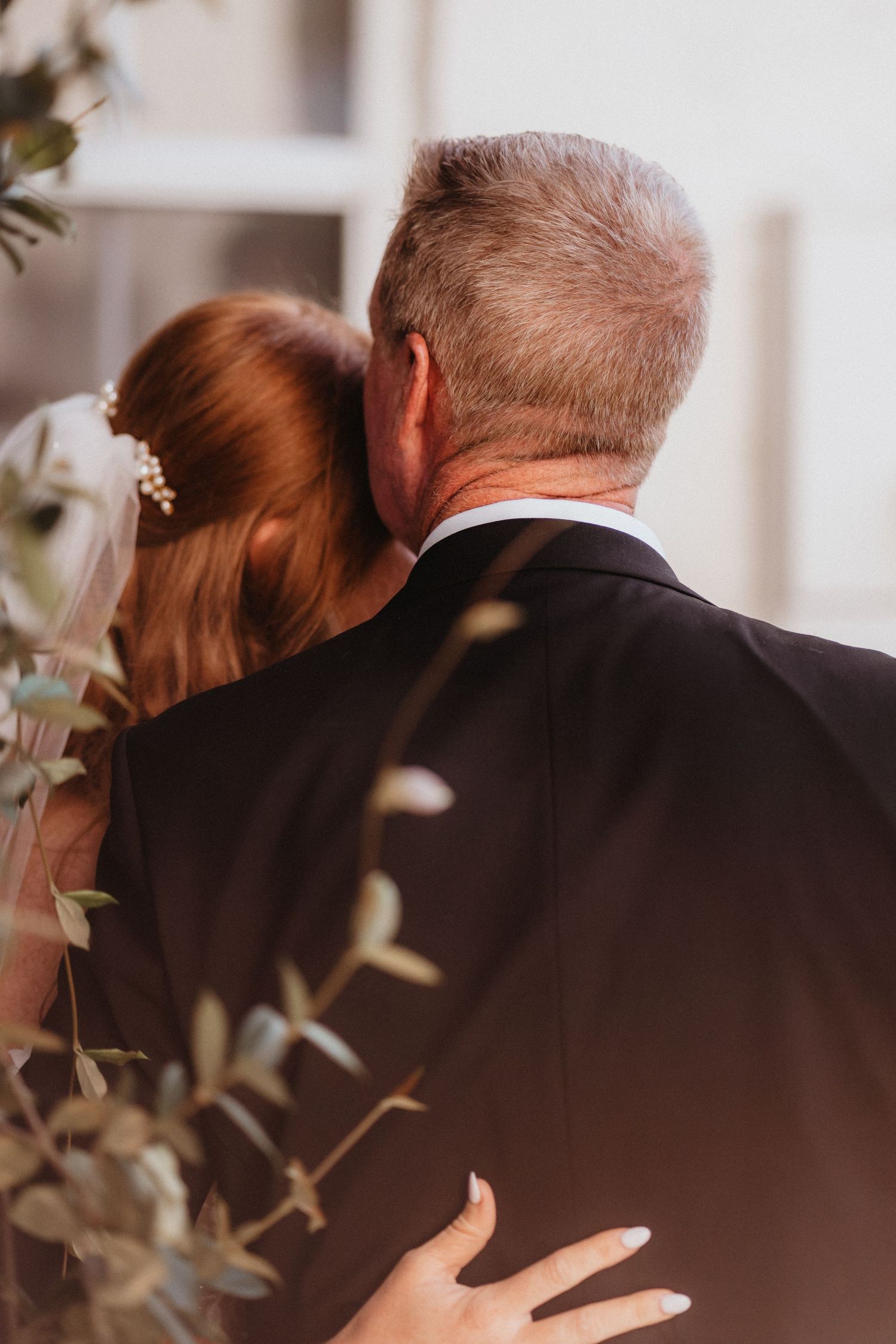 Bride with pearl hair accessories rests her head on fathers shoulder during wedding first look.