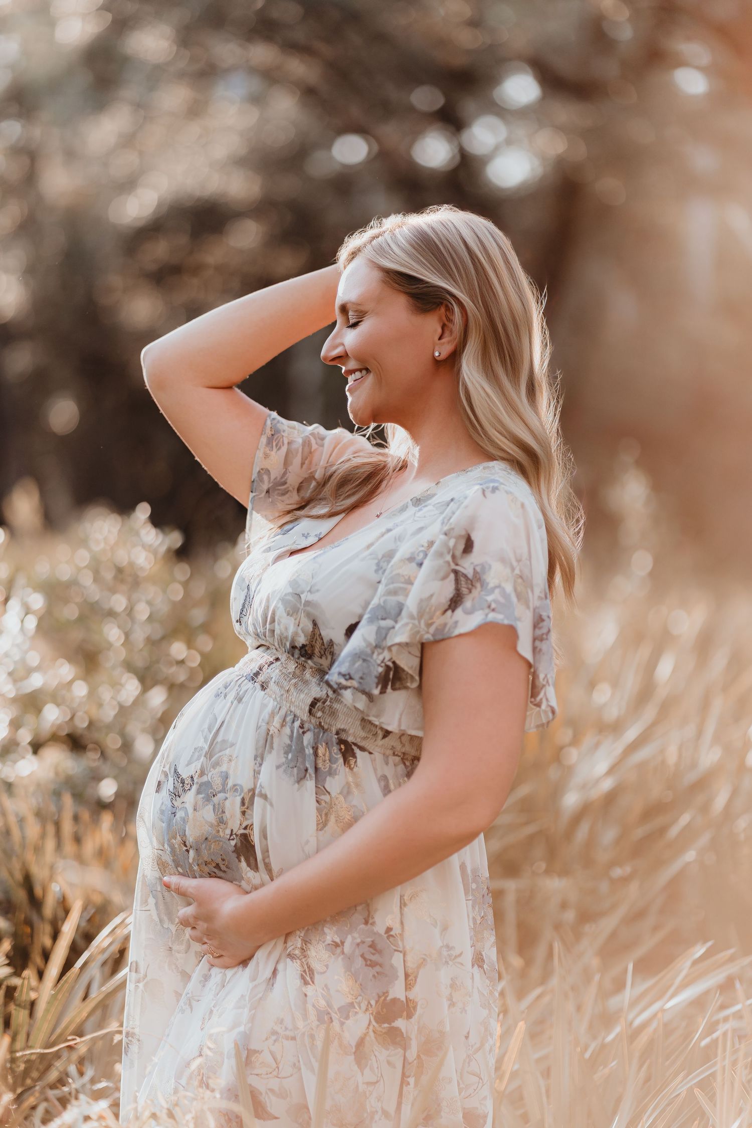 Glowing pregnant woman in floral dress smiling in golden sunlit meadow.