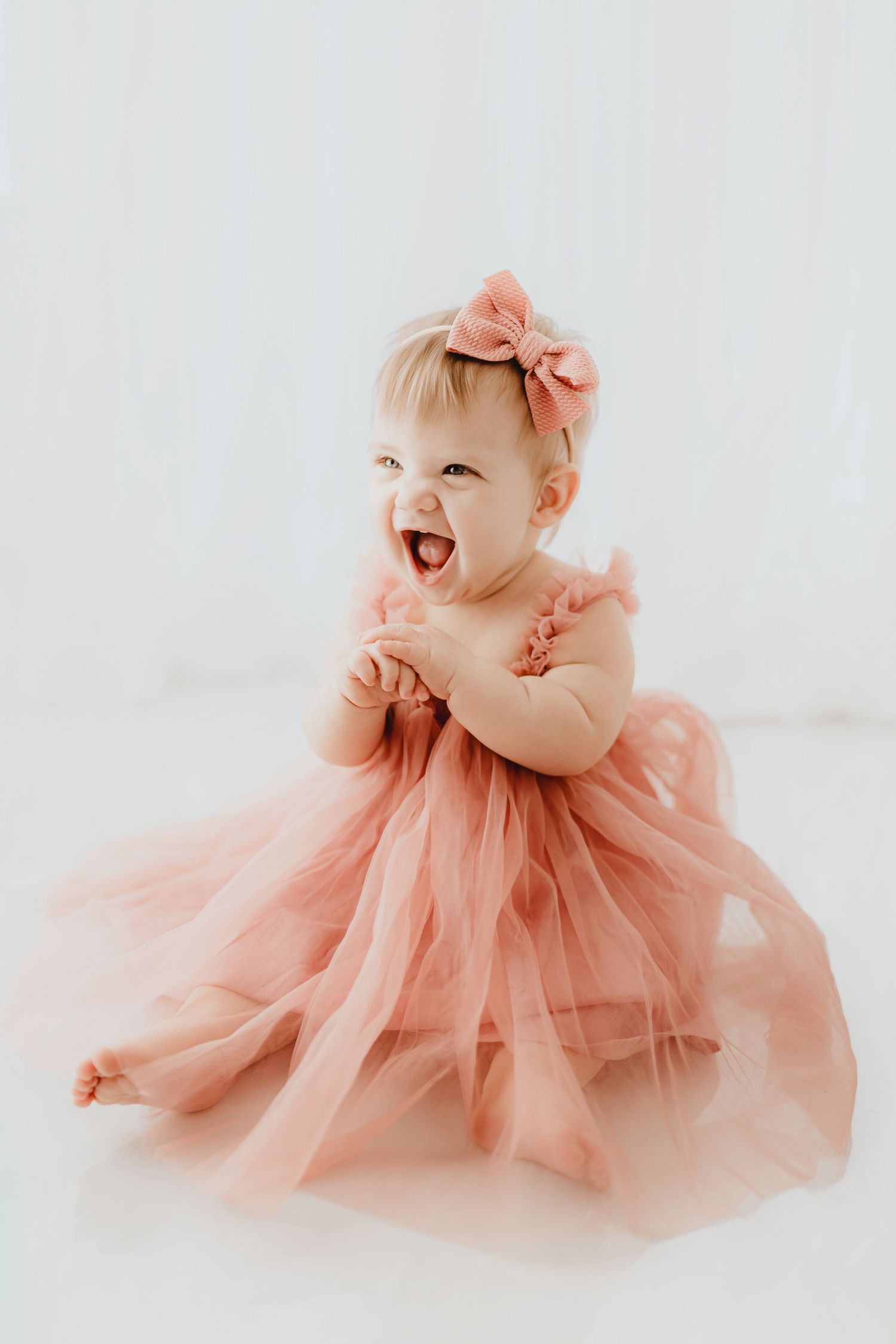 Happy baby girl in dusty rose tulle gown clapping hands with big smile.