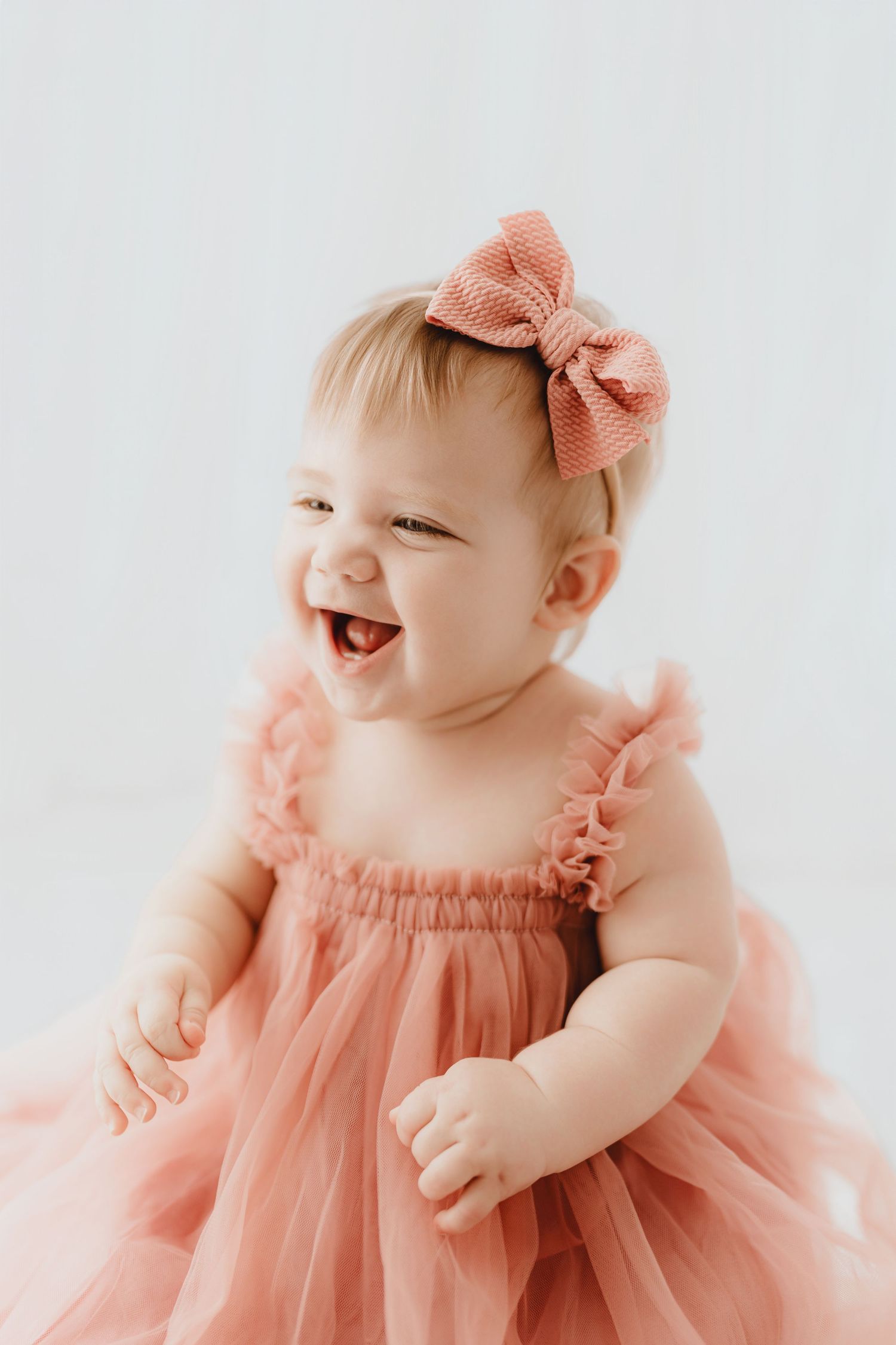 Happy baby girl laughing in pink tulle dress and matching bow headband.