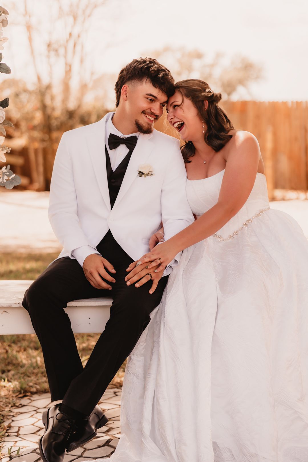 Happy bride and groom sitting together on a bench, smiling and touching foreheads in warm golden light.