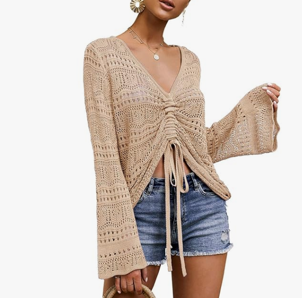 Woman wearing a beige crochet open-knit V-neck drawstring top with flare sleeves paired with denim shorts.