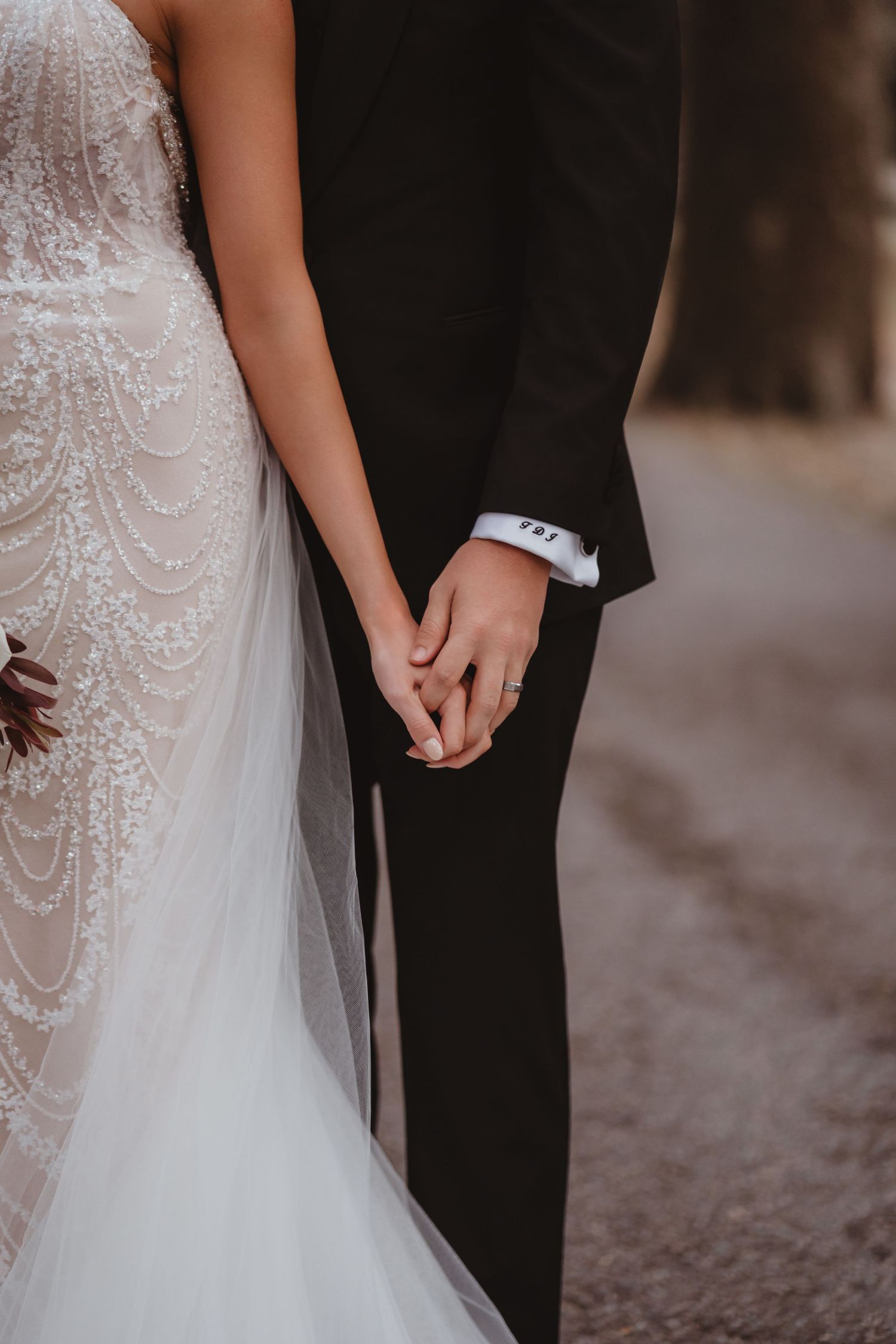 Close-up of bride and groom holding hands, showcasing lace wedding gown and classic black tuxedo.