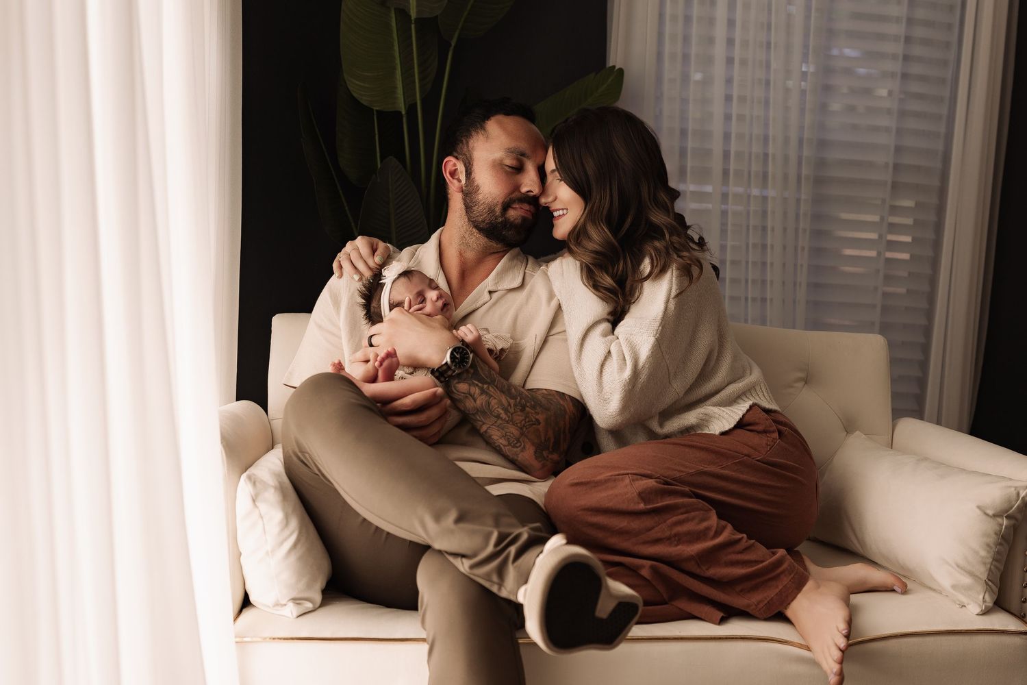 Happy young couple sitting on white armchair sharing a tender moment with their newborn baby.