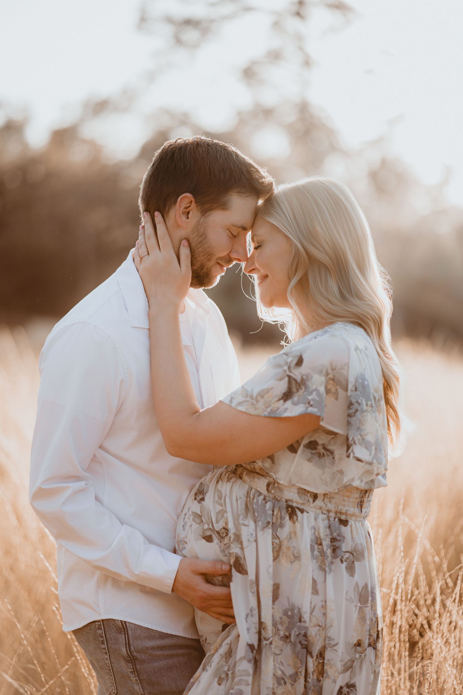 Expectant couple shares tender forehead touch in golden field during romantic outdoor maternity photoshoot.