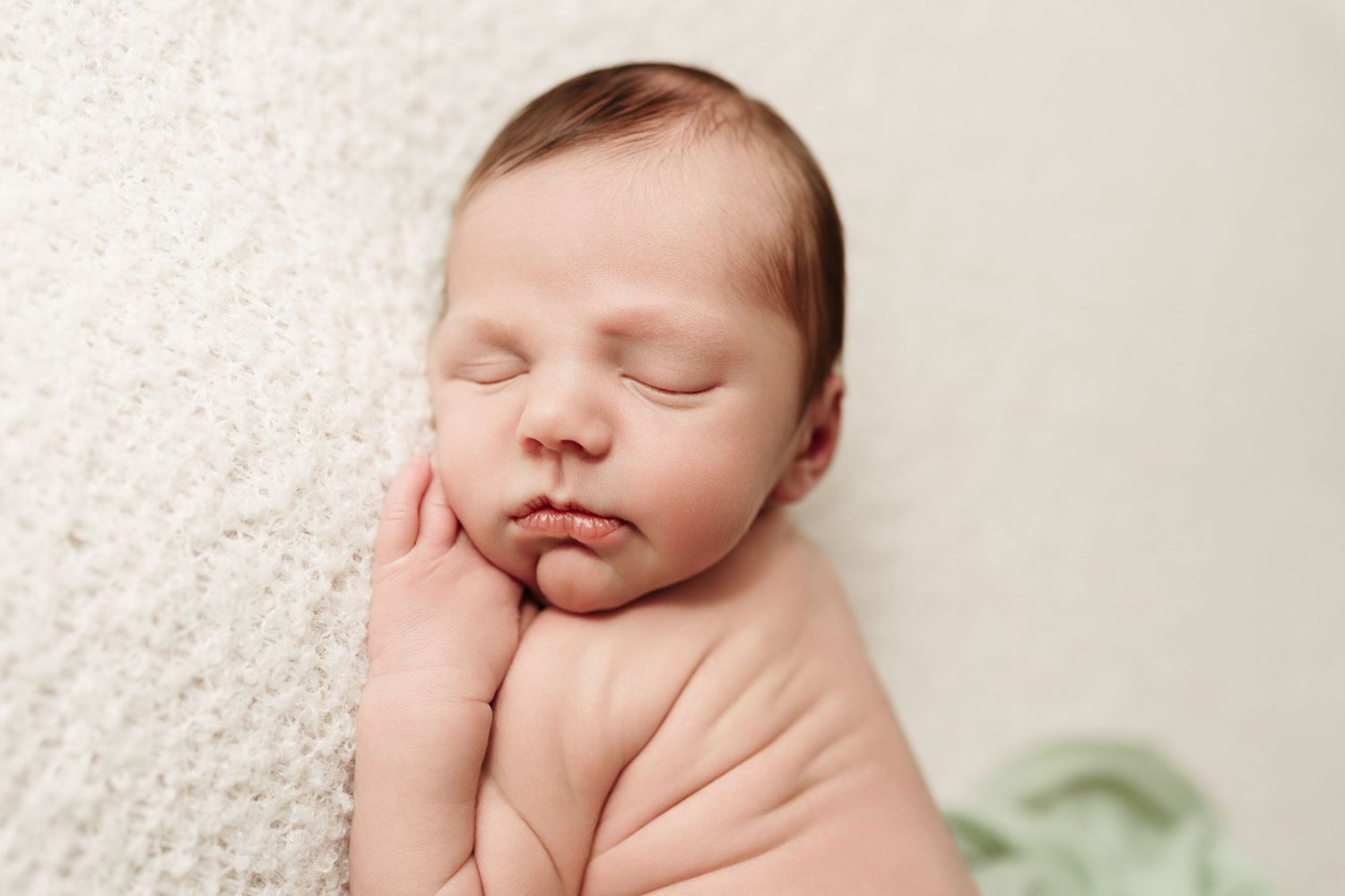 Close-up of sleeping newborn baby resting cheek on hands on cream textured background.