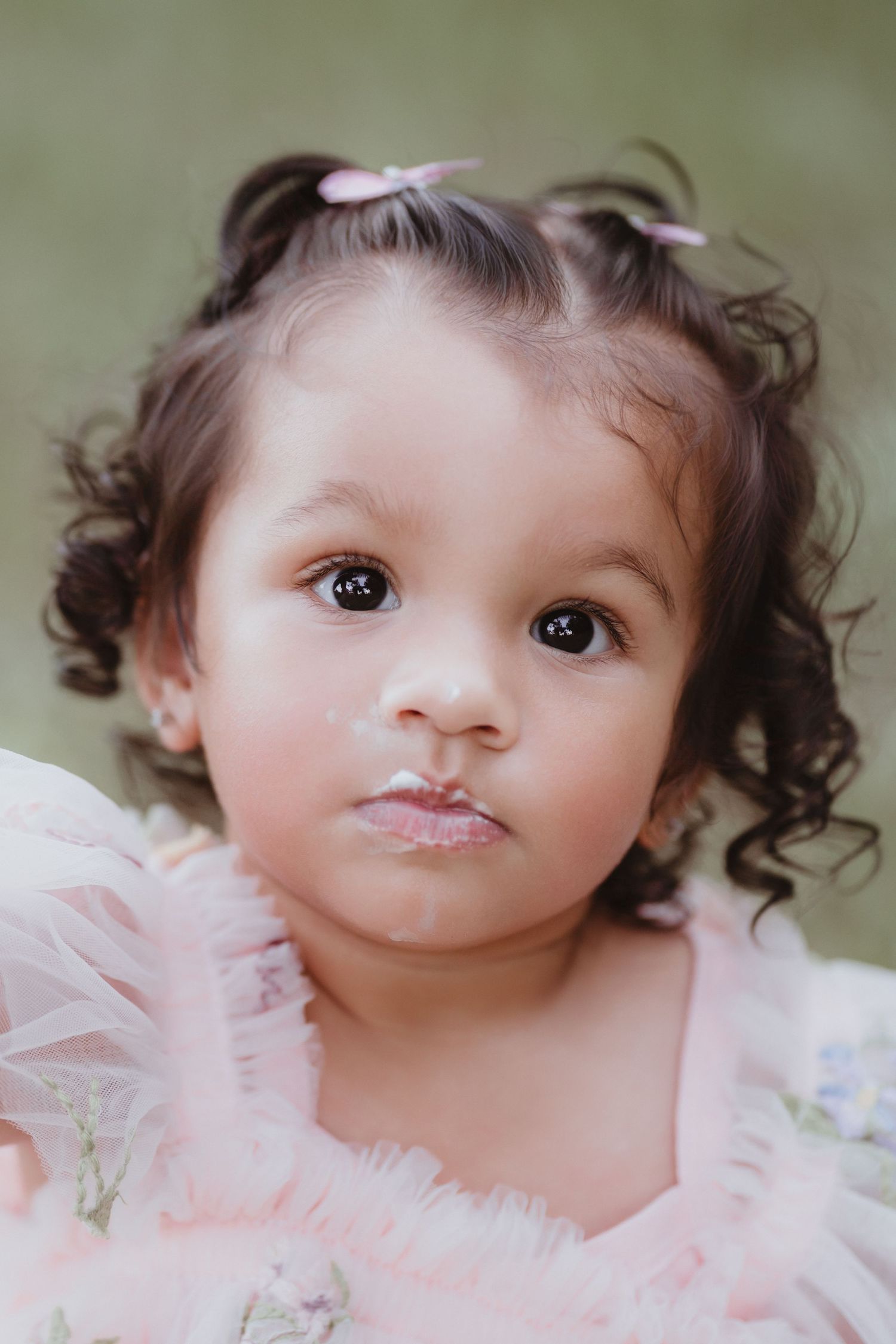 Close-up portrait of toddler girl with curly hair and frosting on her lips.