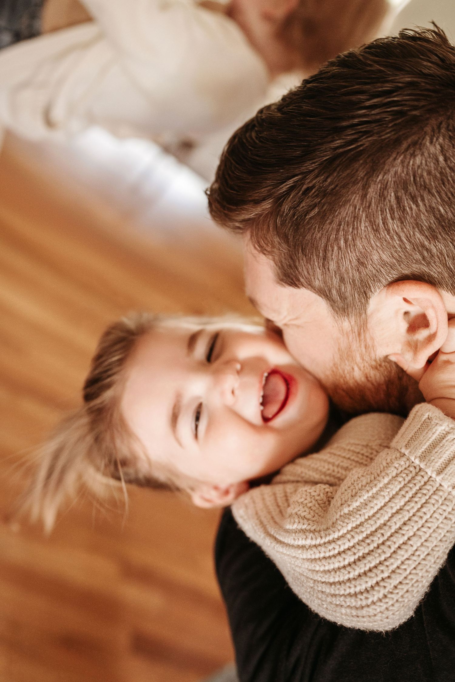 A laughing little girl is kissed on the cheek by her bearded father in a joyful moment.