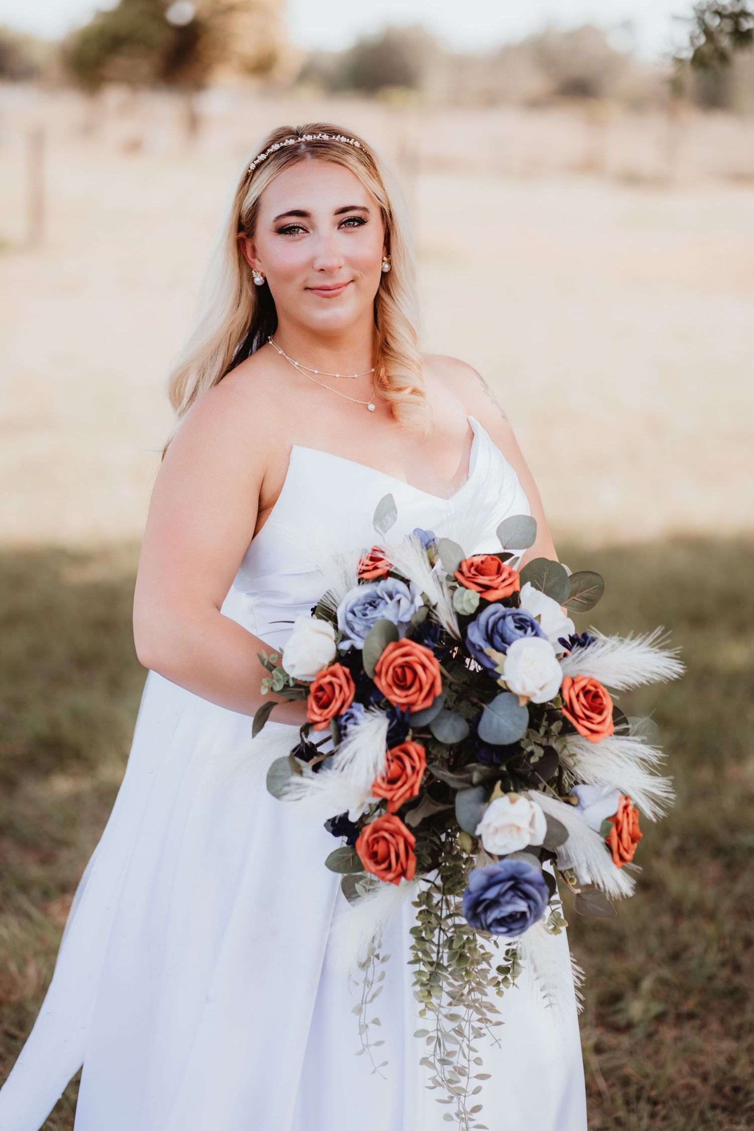 Smiling bride in white strapless gown holding cascading bouquet of orange, lavender, and white roses.