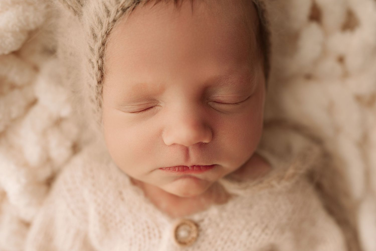 Close-up portrait of a sleeping newborn baby in a cream knit hat and outfit.