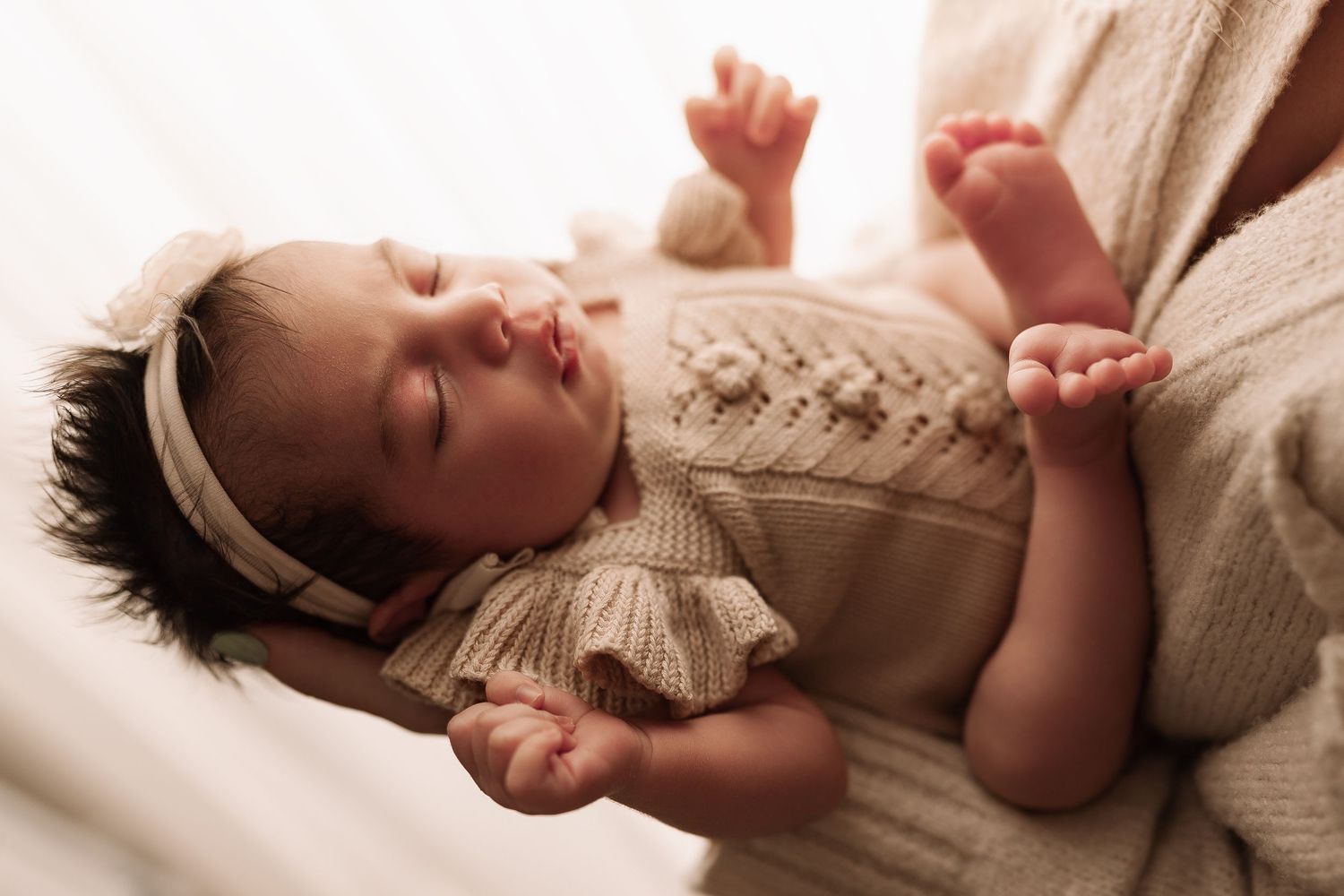 Peaceful newborn baby sleeping in a knit romper and white headband, lying on a soft blanket.