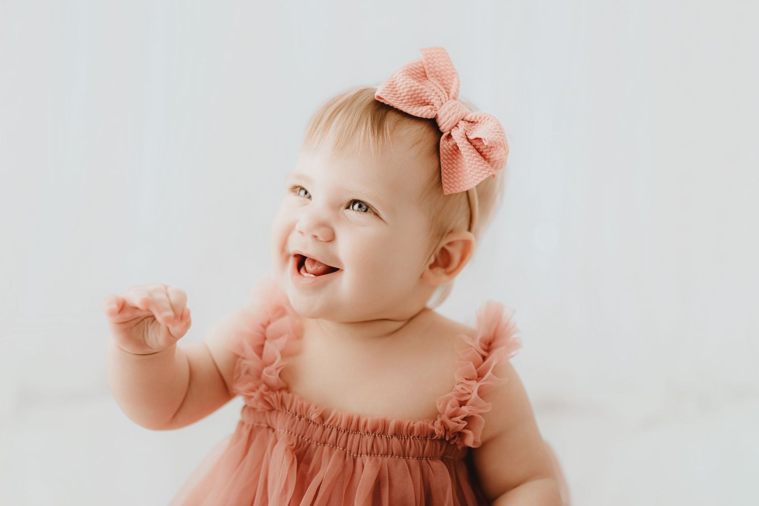 Laughing baby girl in pink tulle dress and bow headband.