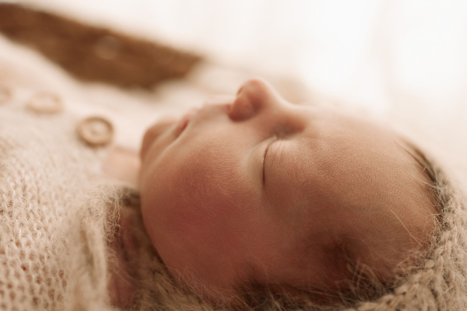 Close-up of a sleeping newborn baby in a soft beige knit wrap with buttons.